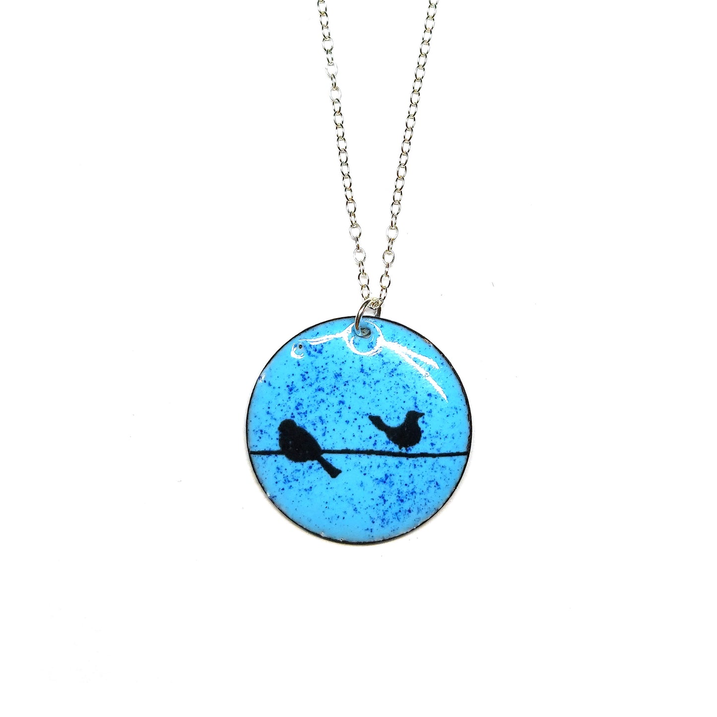 Round enamel pendant with bird silhouettes sat on a wire against a blue background. Suspended on a silver chain.