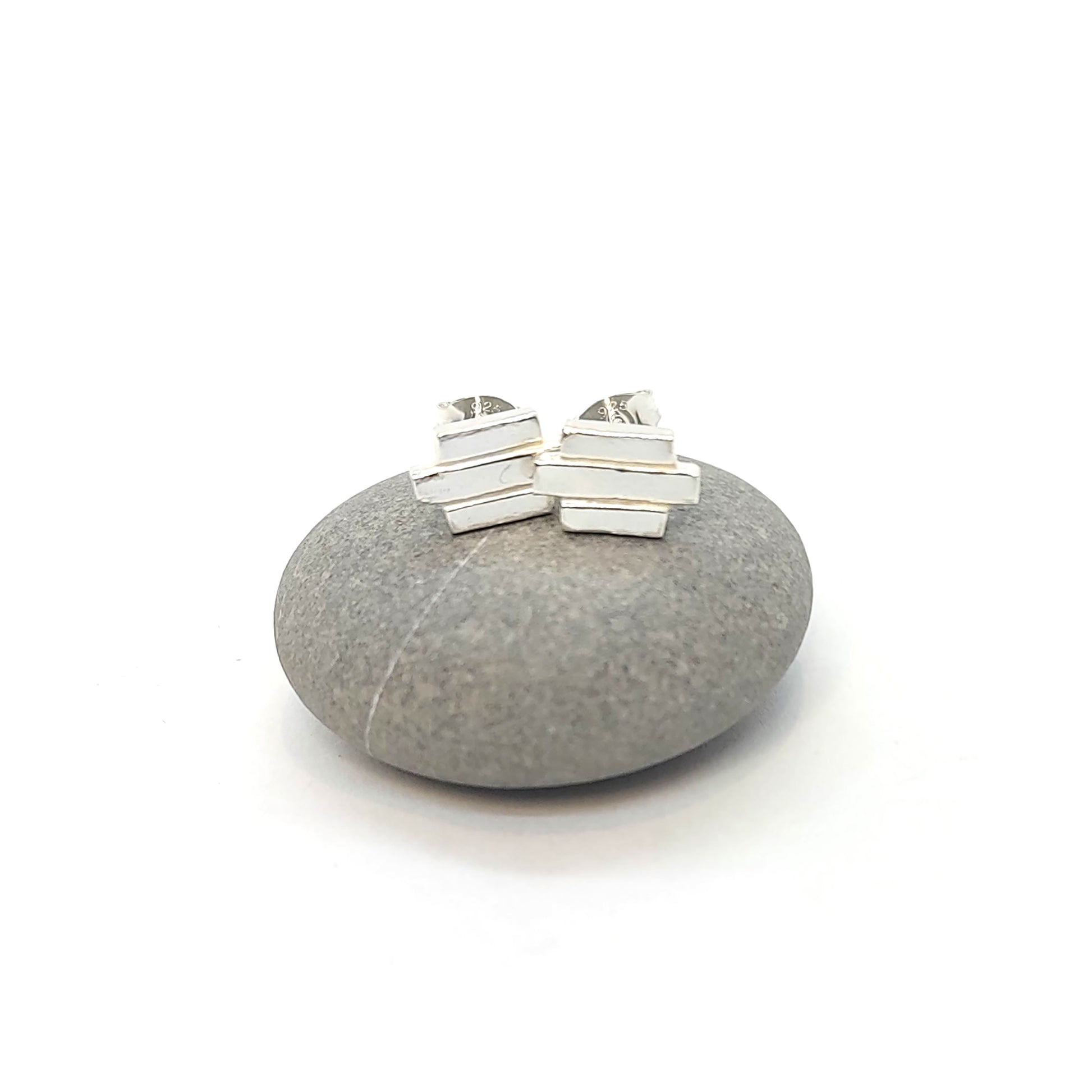 Silver Art Deco style stud earrings featuring 3 lines of silver. Pictured on a pebble.