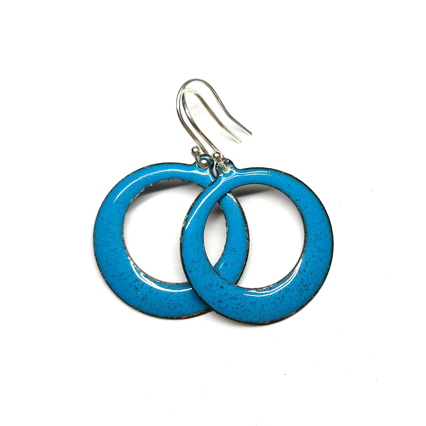 Enamel drop earrings featuring an open circle with teal enamel and a dusting of red enamel. On silver ear hooks.