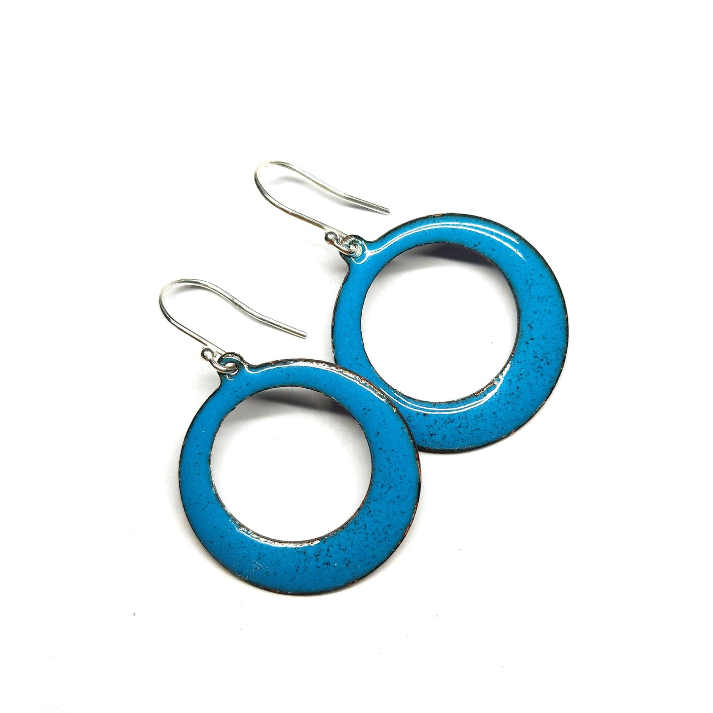 Enamel drop earrings featuring an open circle with teal enamel and a dusting of red enamel. On silver ear hooks.