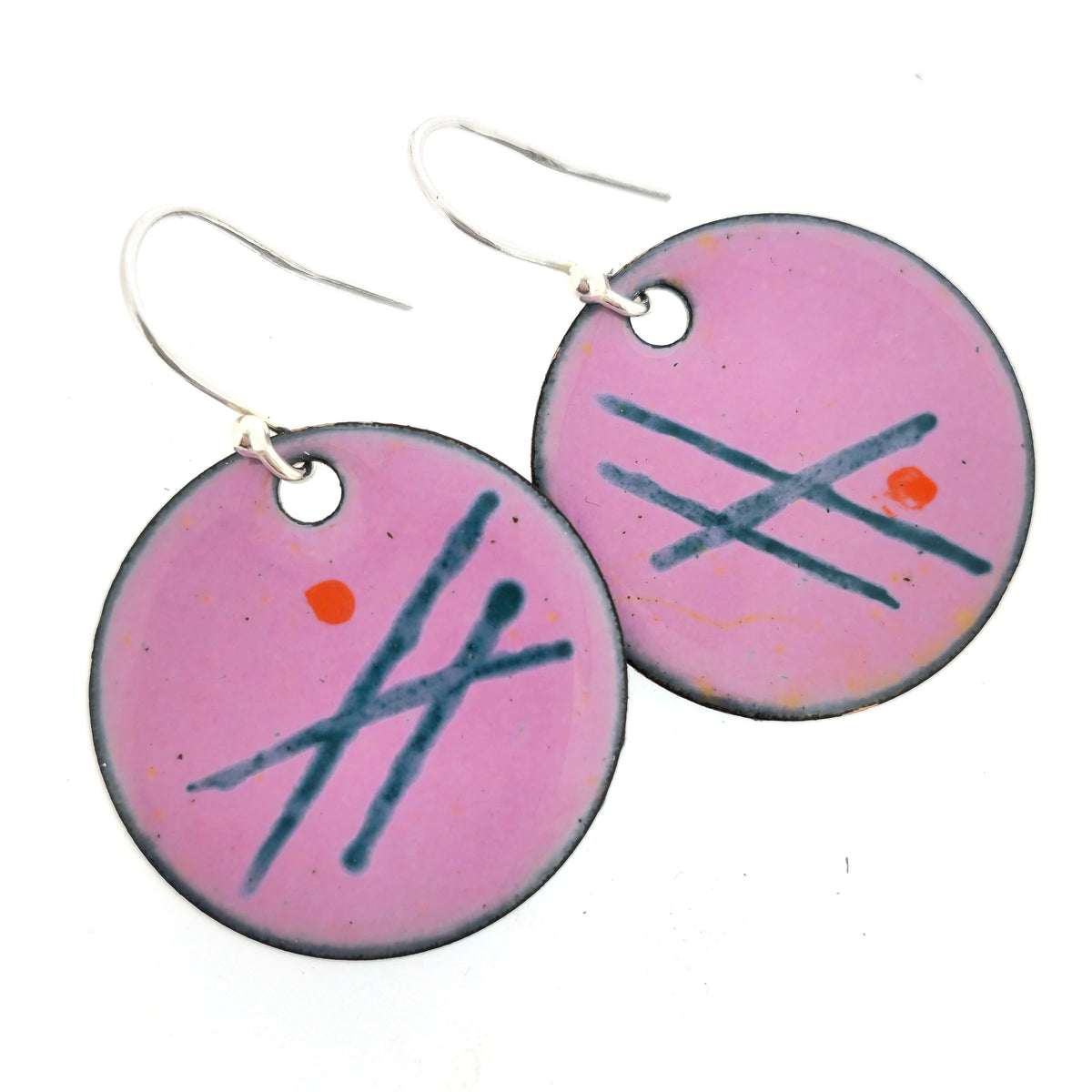 A pair of handmade round pink enamel drop earrings with green lines and orange dots. On silver ear hooks. On a white background. Mijoux jewellery.