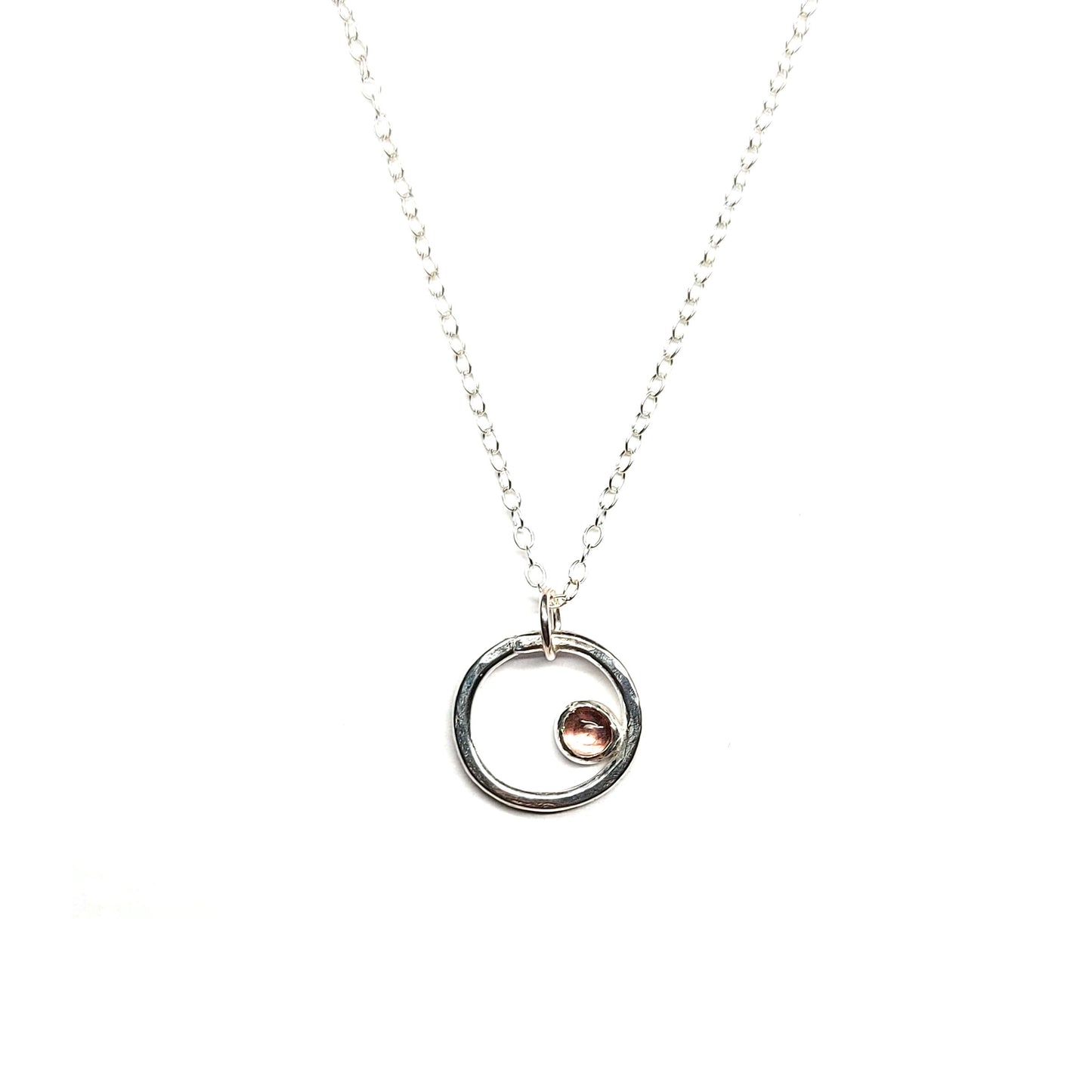 Silver hammered open circle pendant with round pink tourmaline gemstone set off-centre. On a silver chain.