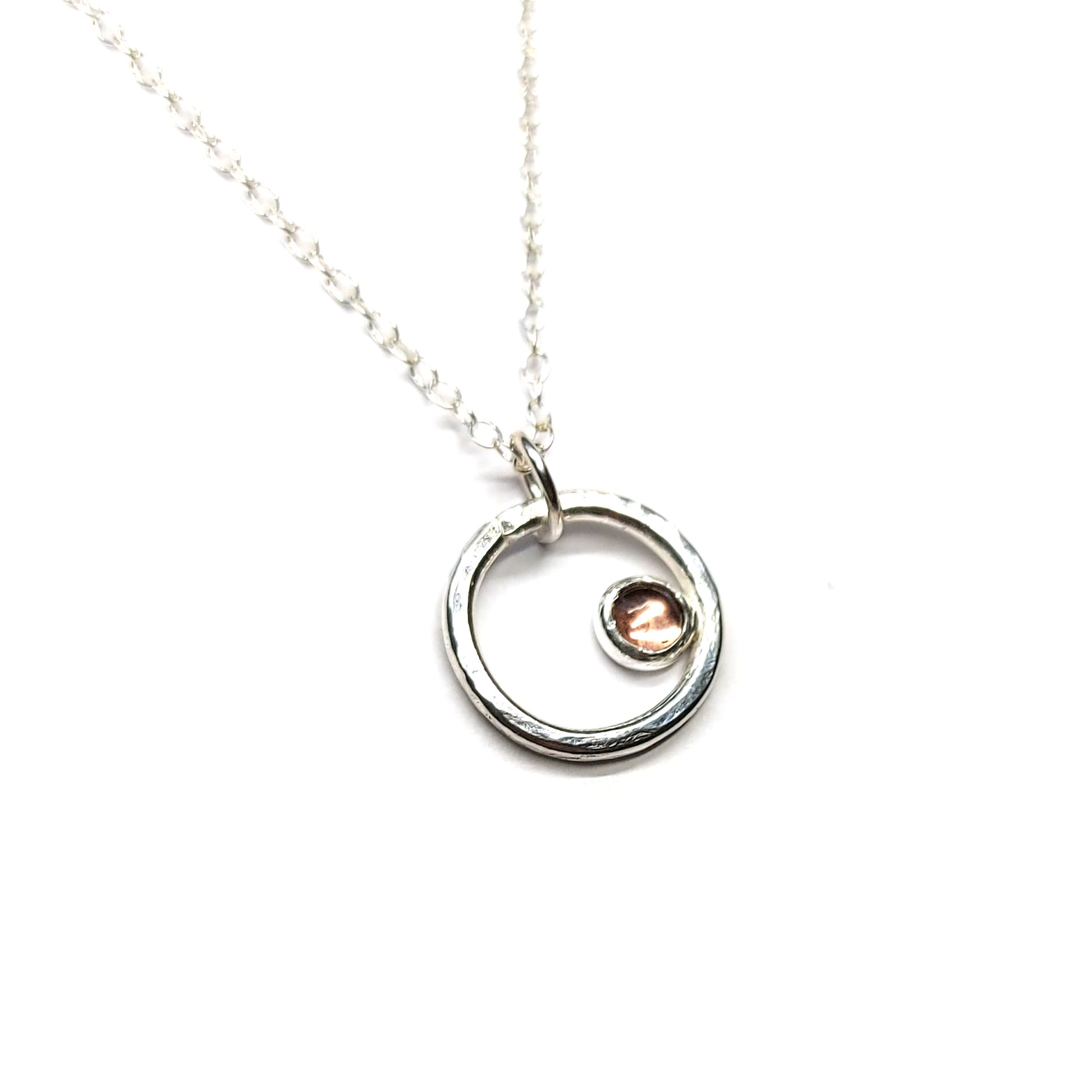 Silver hammered open circle pendant with round pale pink tourmaline gemstone set off-centre. On a silver chain.