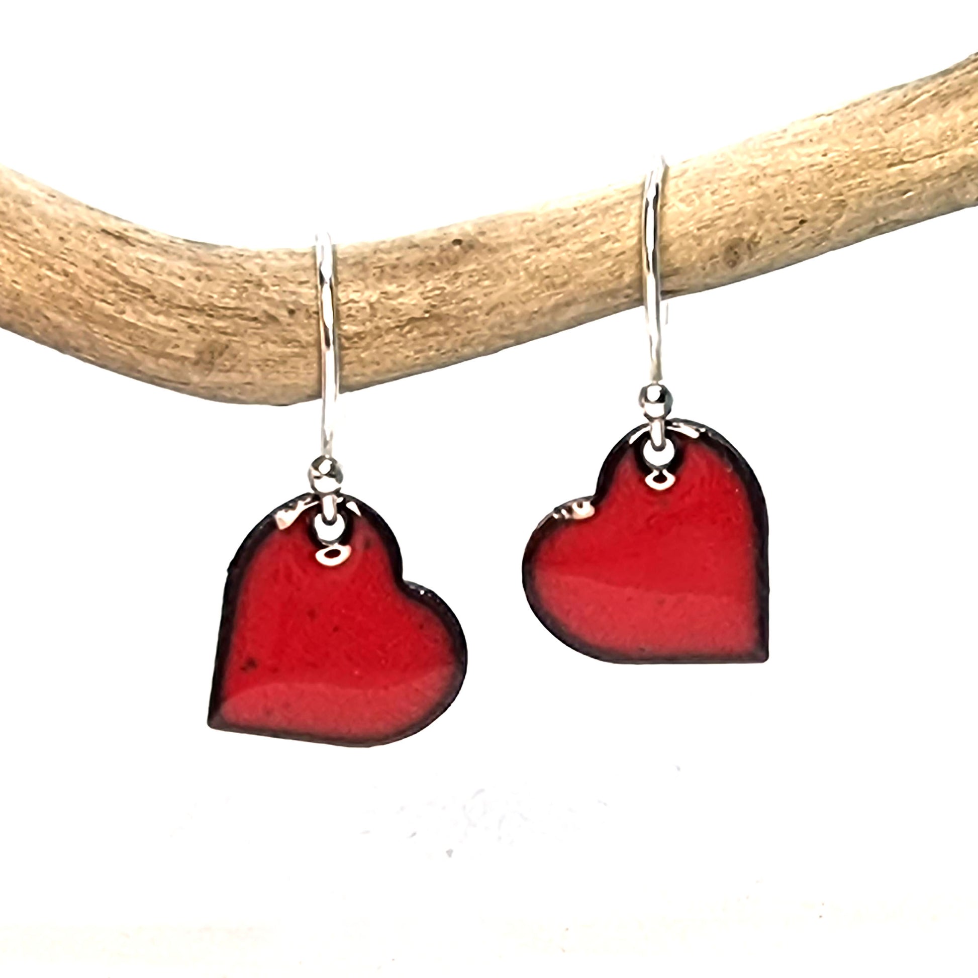 Red enamel heart drop earrings suspended on a twig