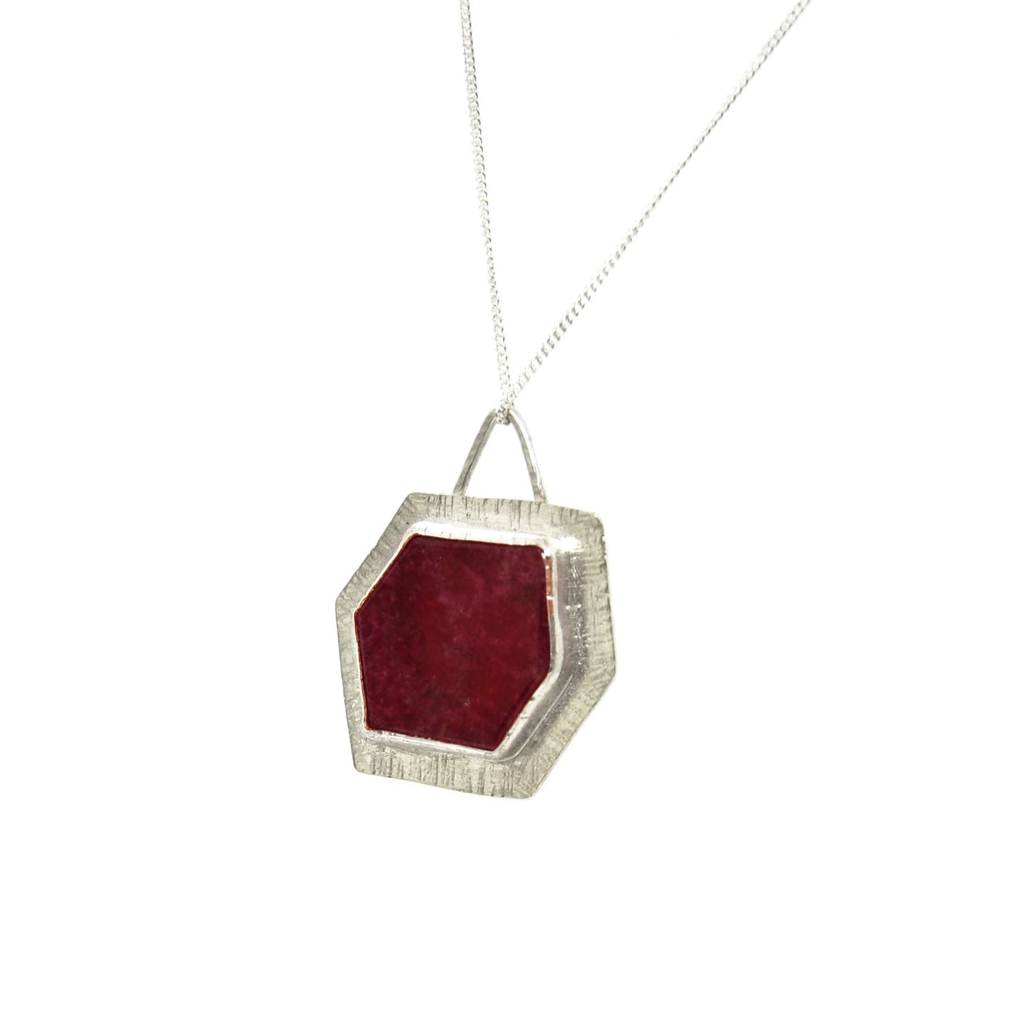 A silver pendant with a hexagonal ruby slice set into a textured surround. On a silver chain.