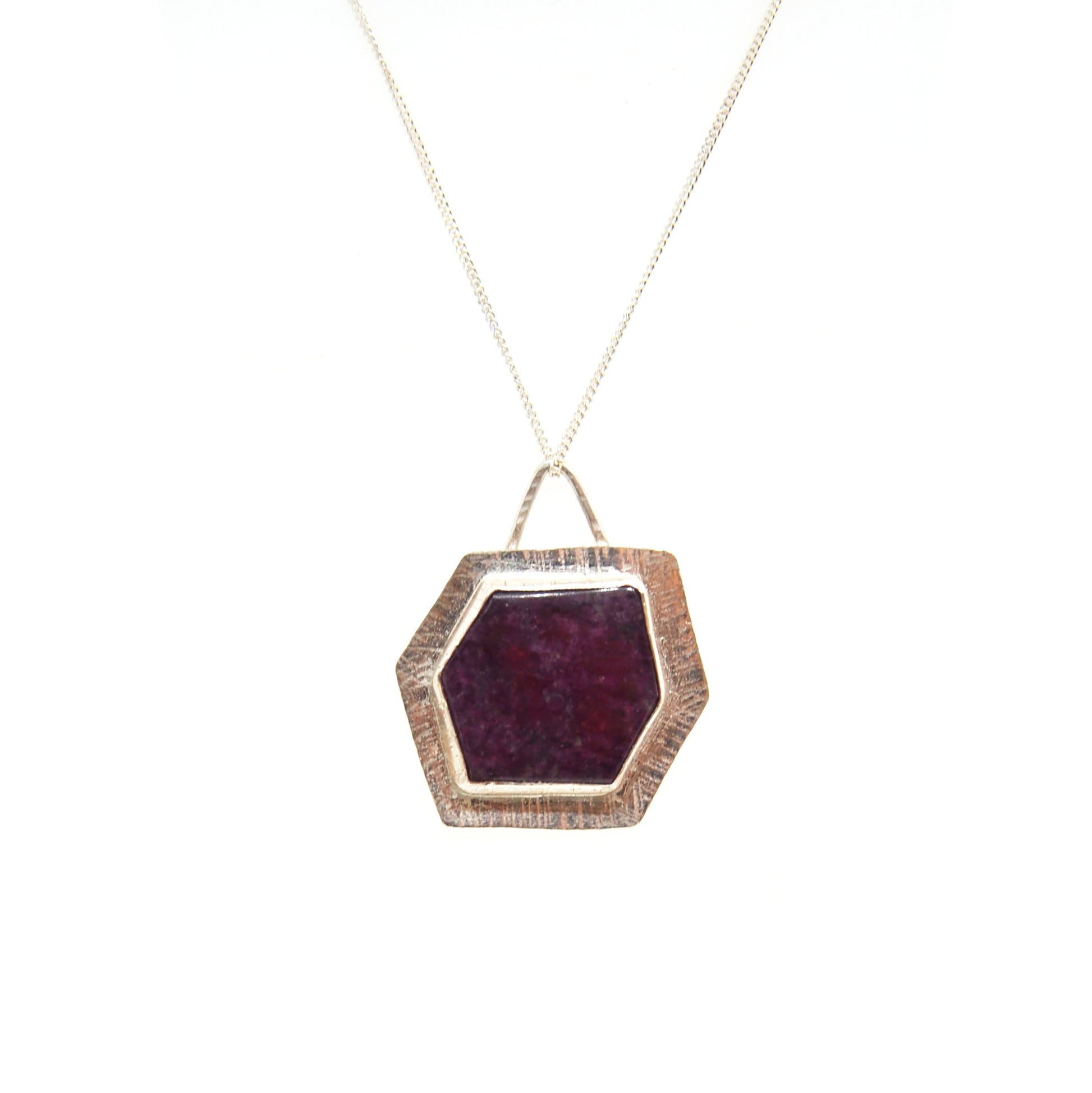 A silver pendant with a hexagonal ruby slice set into a textured surround. On a silver chain.