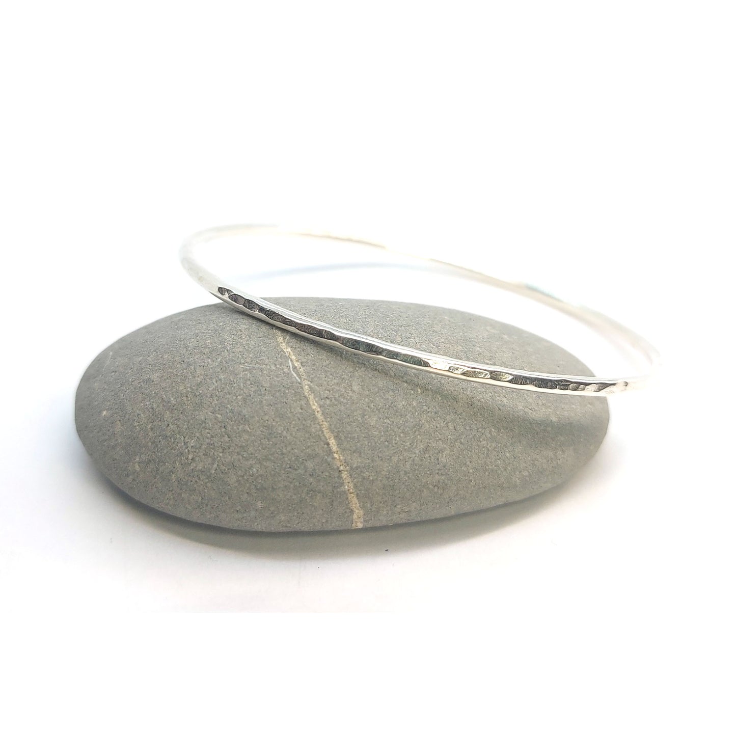 Silver hammered bangle on pebble