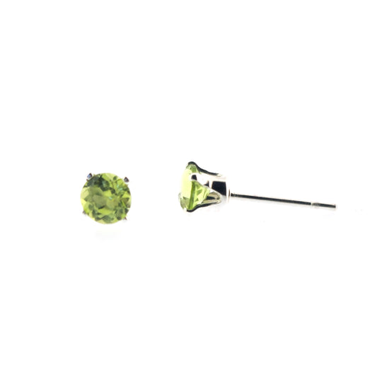 Silver stud earrings with light green round faceted peridot gemstones in a 4 claw setting. 1 in front view, 1 in side view.