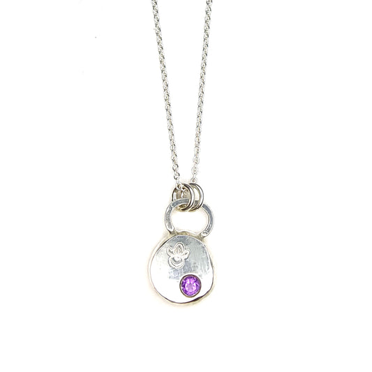 A round silver pendant with a violet flower (February birth flower) engraved on it and a round purple amethyst (February birthstone) flush set into it. On a silver chain.