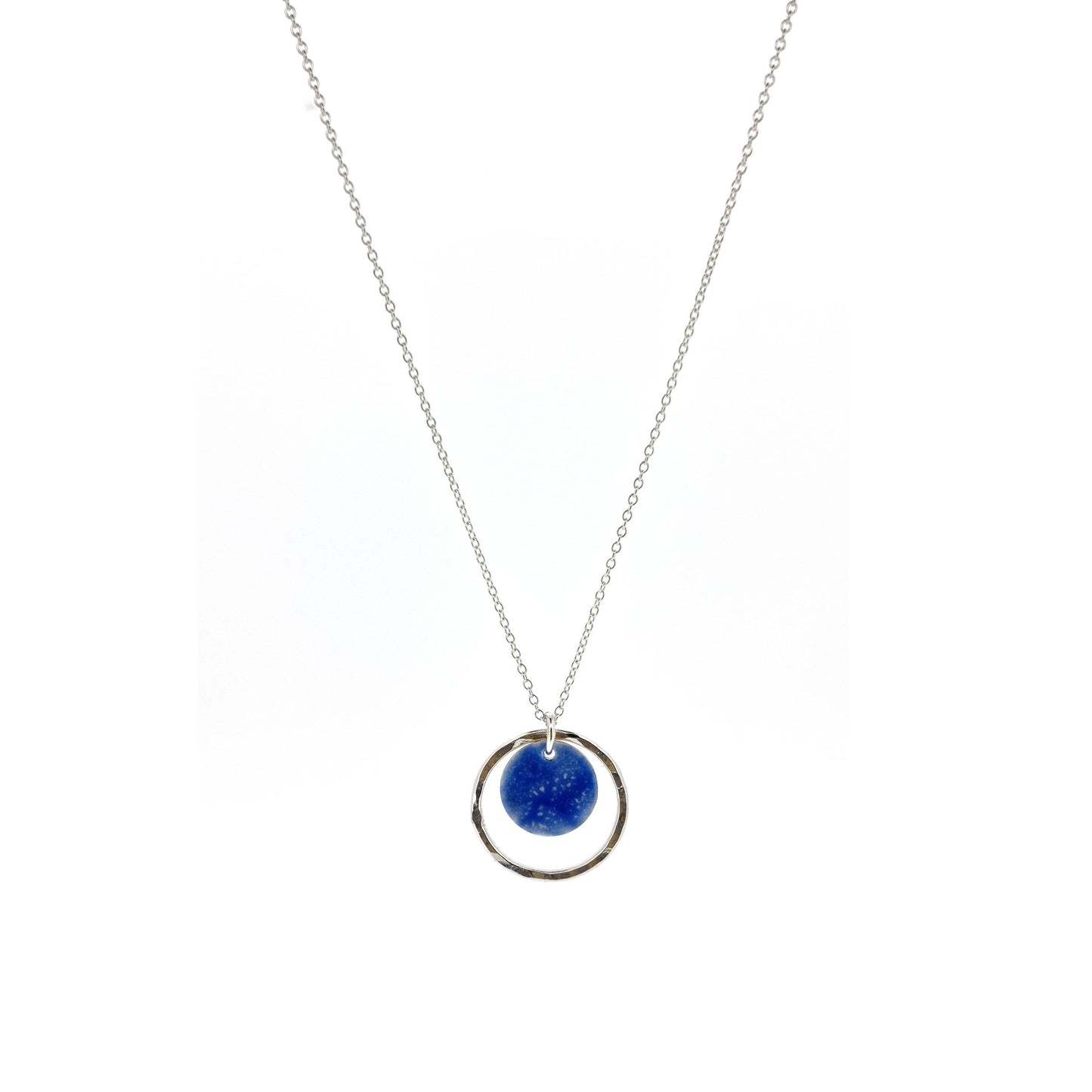 A silver pendant with a central disc with a blue patterned enamel surrounded by a silver hammered open circle. On a silver chain.