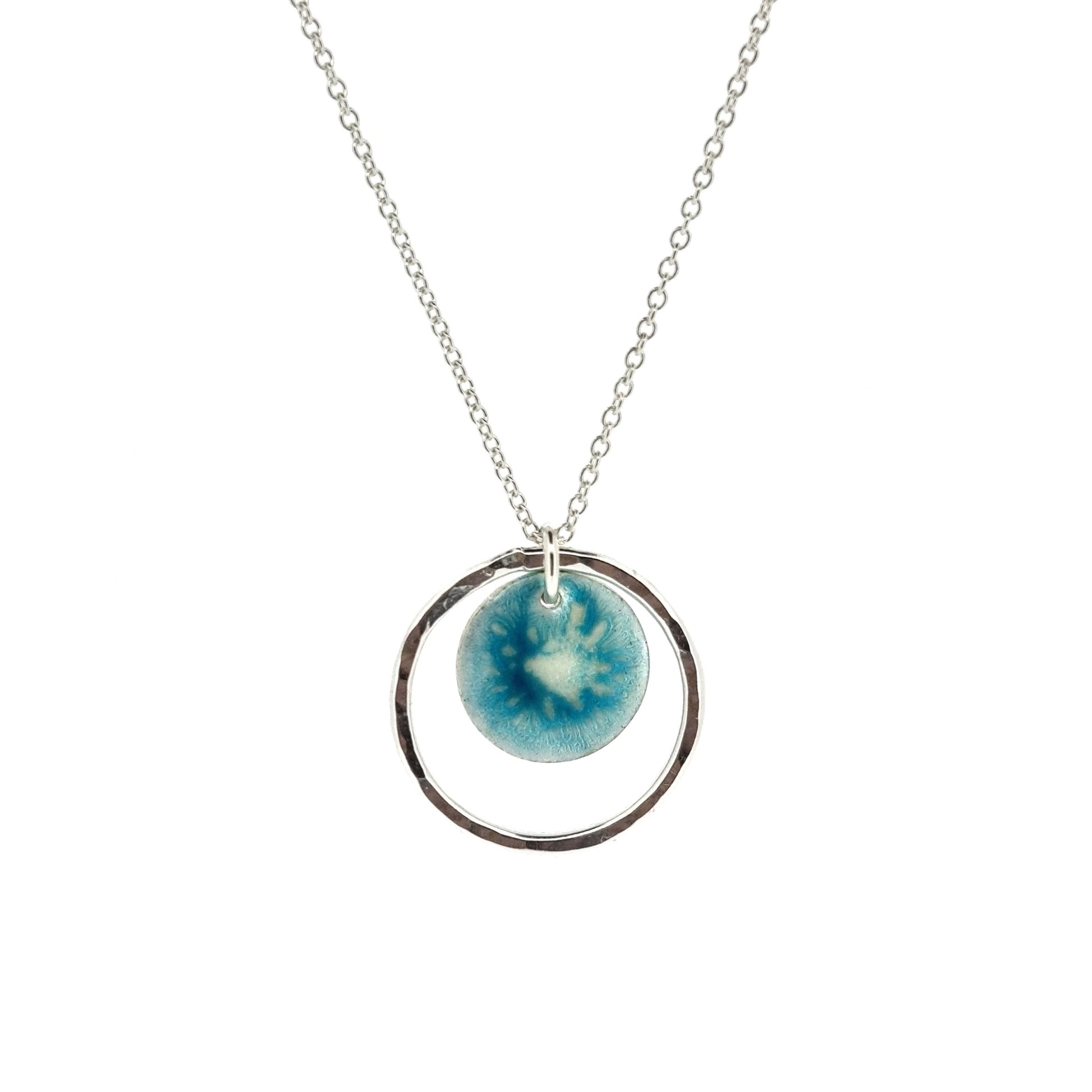 Silver pendant with a central silver disc covered with a turquoise enamel pattern and a surrounding hammered silver circle. On a silver chain.