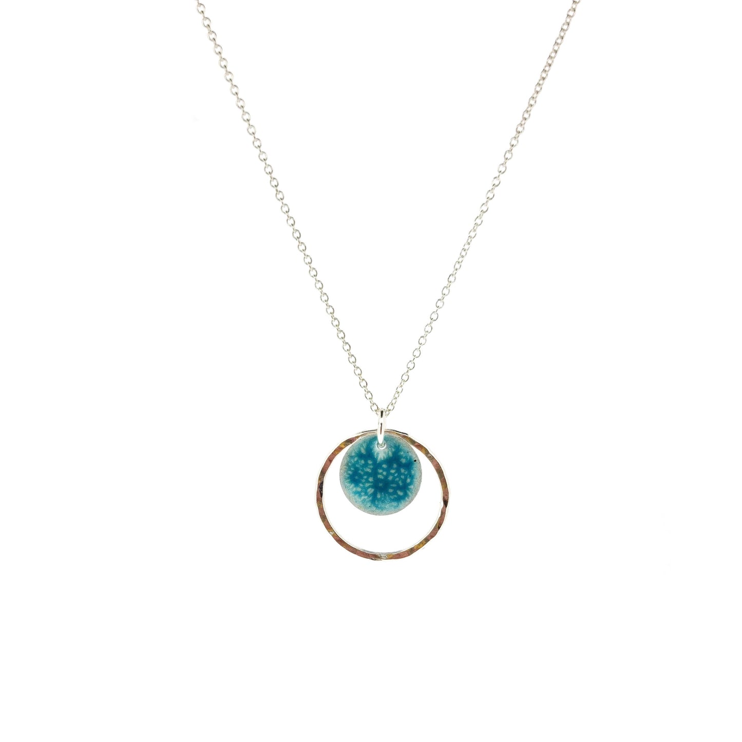 Silver pendant with a central silver disc covered with a turquoise enamel pattern and a surrounding hammered silver circle. On a silver chain.