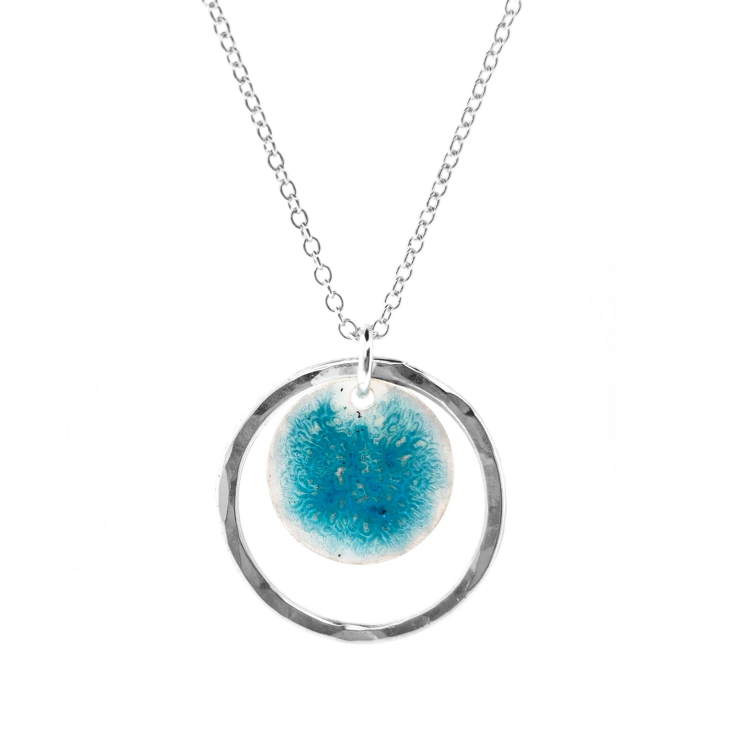 Silver pendant with a central silver disc covered with a turquoise enamel pattern and a surrounding hammered silver circle. On a silver chain.
