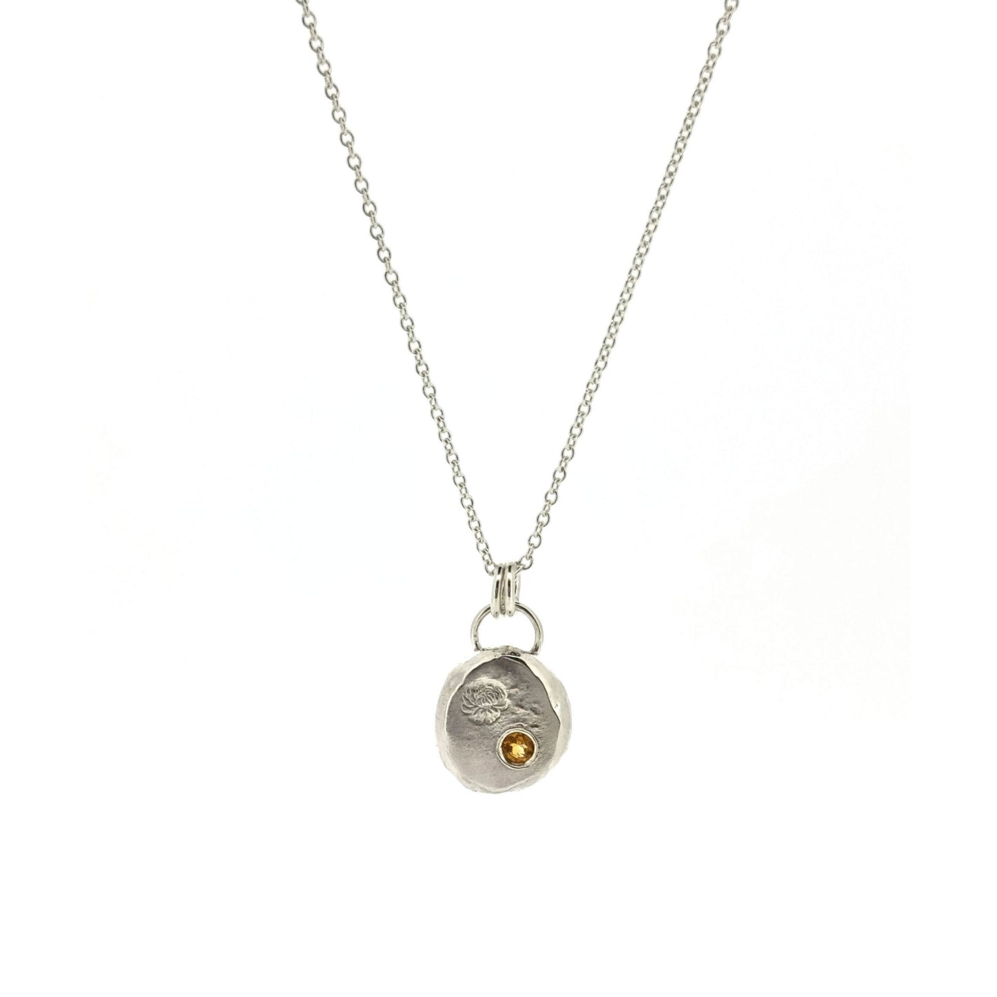Round silver flat pebble pendant with chrysanthemum flower engraved on it and a flush set yellow citrine gemstone. On a silver chain.