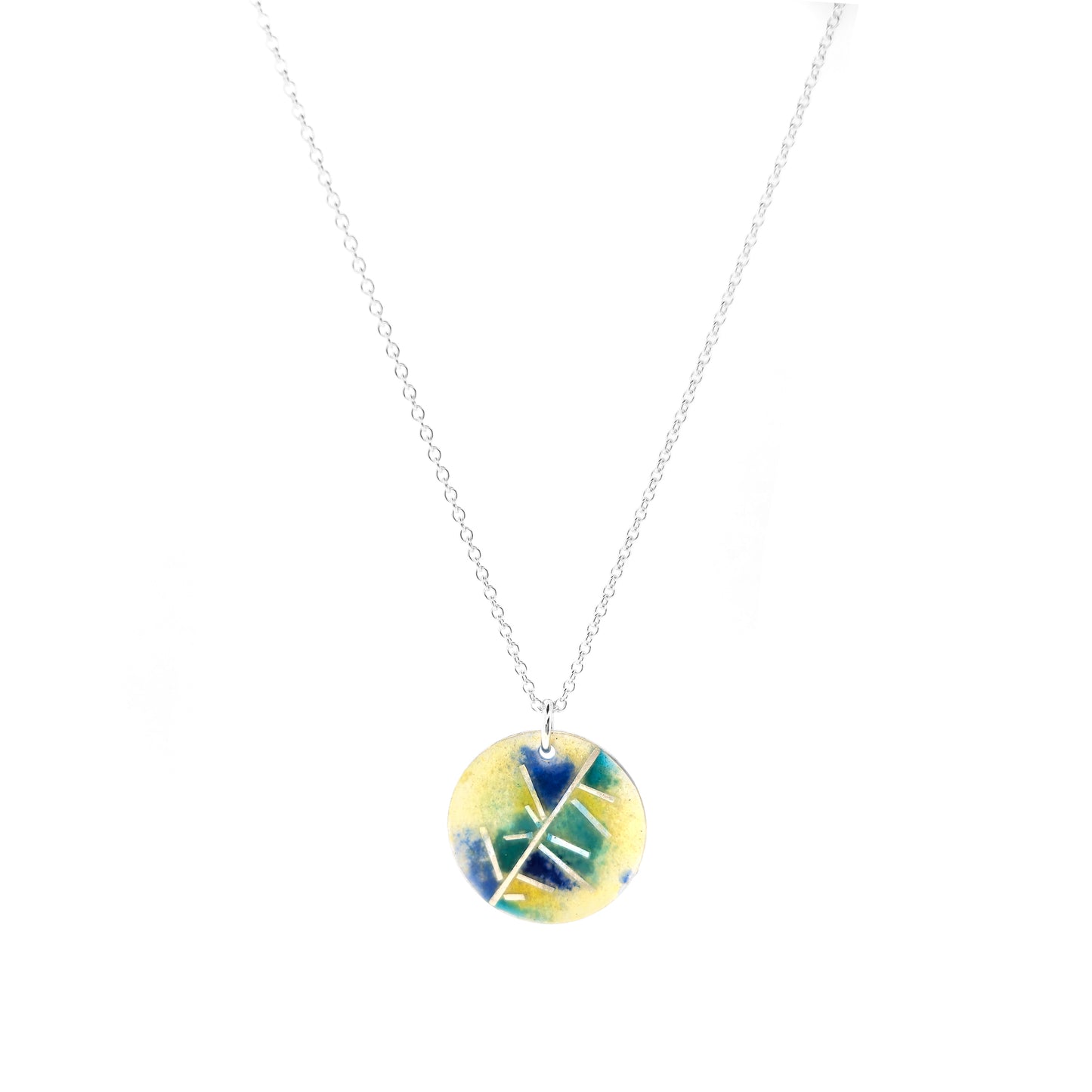 A round silver pendant with abstract silver lines and blue and turquoise enamels blending into pale yellow. Suspended from a silver chain. Small.