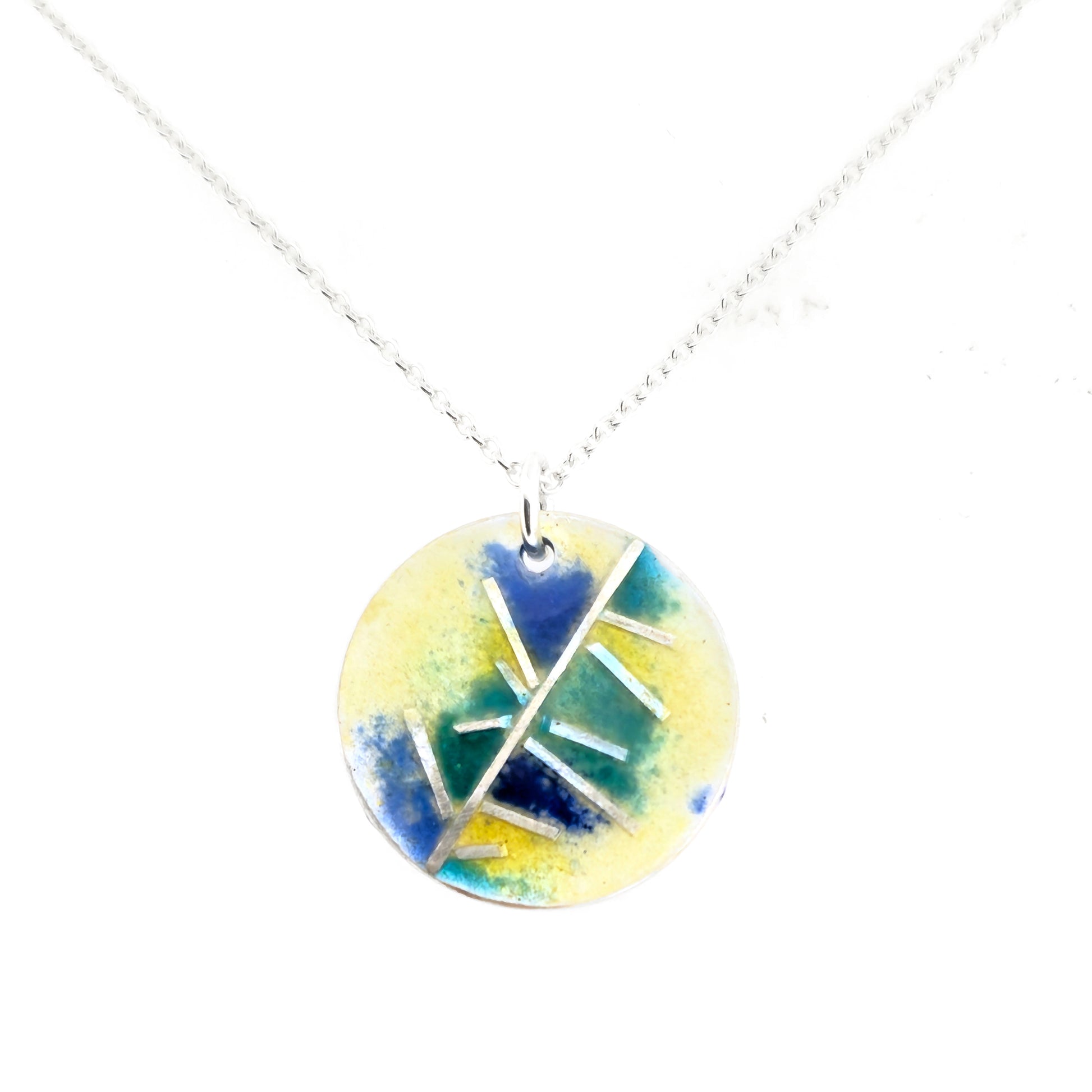 A round silver pendant with abstract silver lines and blue and turquoise enamels blending into pale yellow. Suspended from a silver chain.  Small.