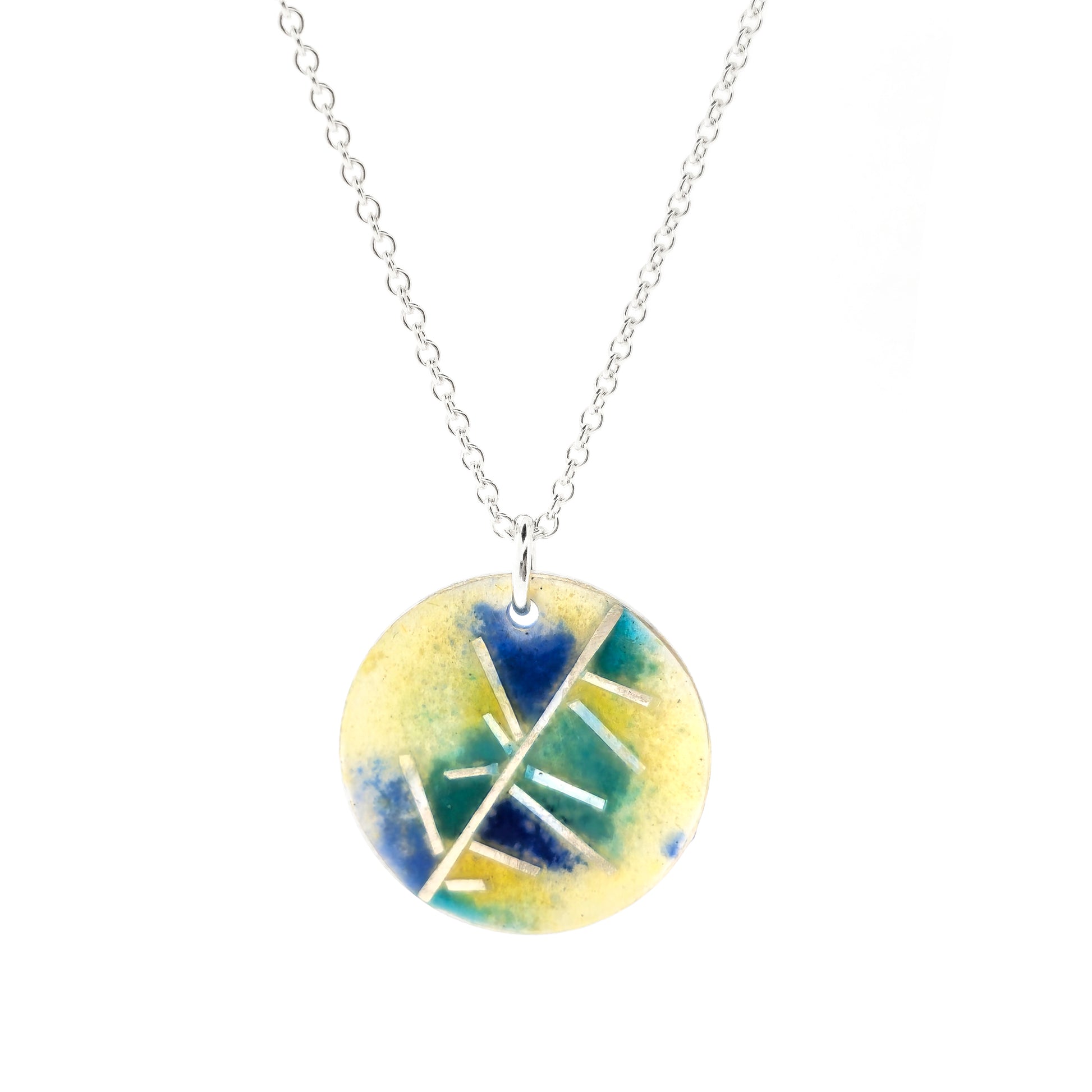 A round silver pendant with abstract silver lines and blue and turquoise enamels blending into pale yellow. Suspended from a silver chain. Small.