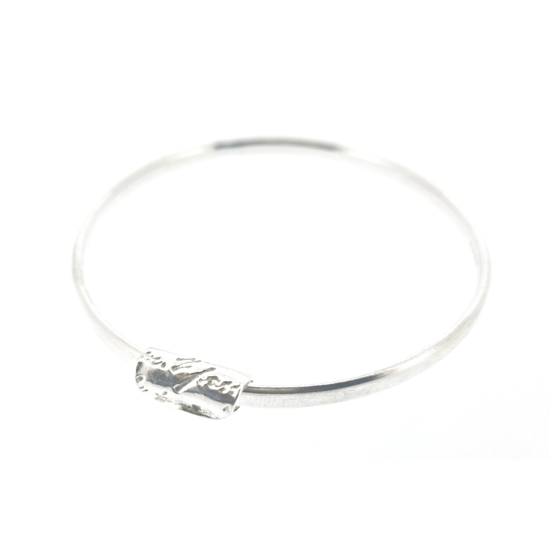 A round silver bangle with an oval profile and a bead with script writing on.