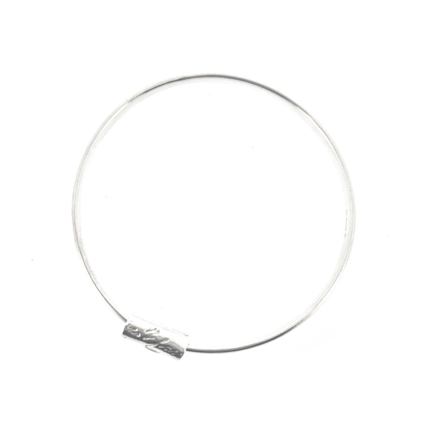 A round silver bangle with an oval profile and a bead with script writing on.