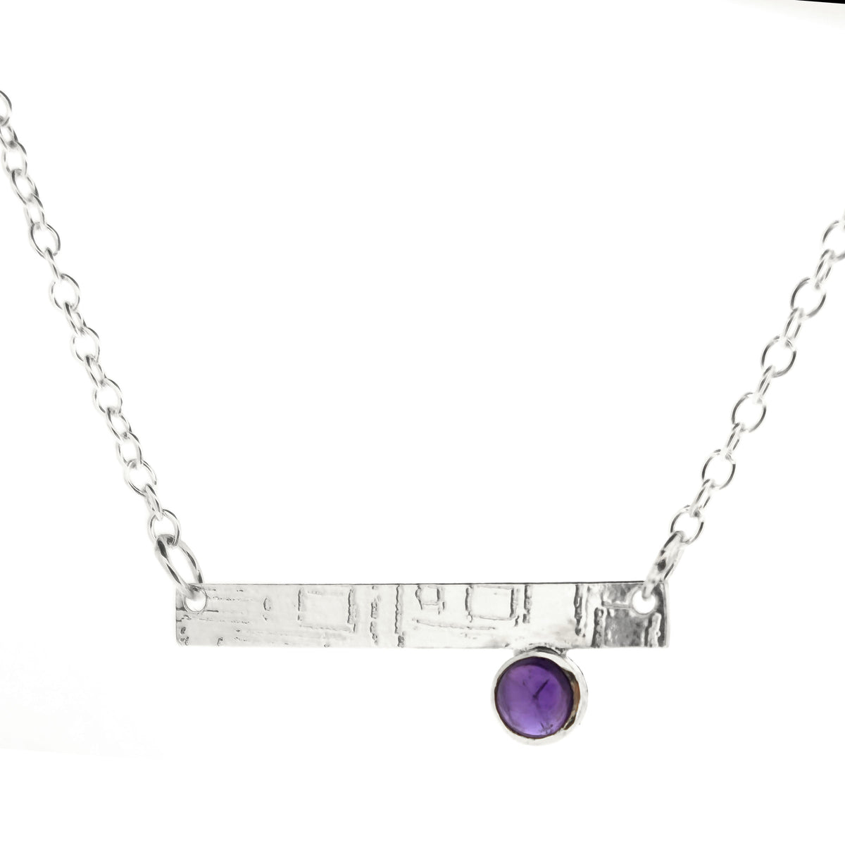 A handmade silver bar necklace with a textured horizontal bar and a small bezel-set purple amethyst stone, shown on a plain white background. Mijoux Jewellery.