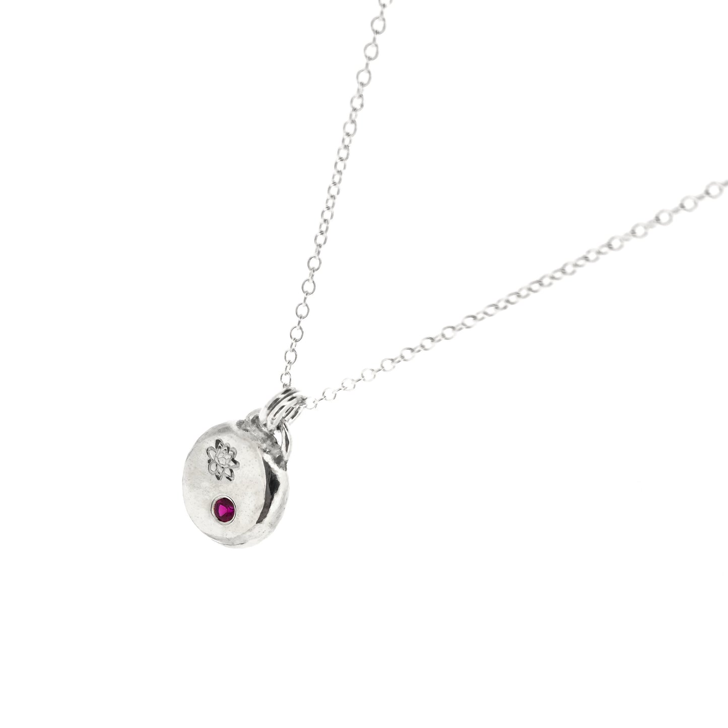 A round silver flat pebble pendant with an engraved lotus flower and flush set red ruby gemstone.
