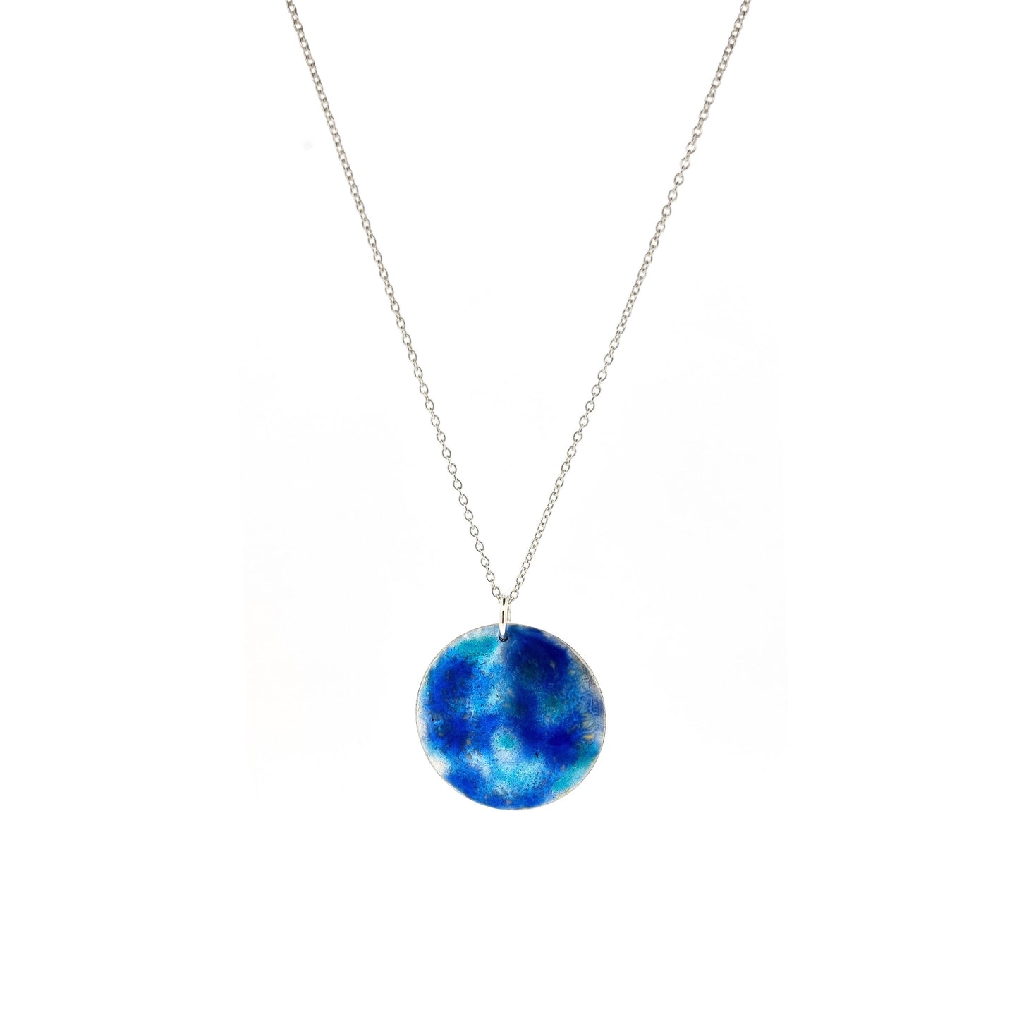 A round silver pendant with a mix of blue and turquoise enamel galaxy pattern on a silver chain.