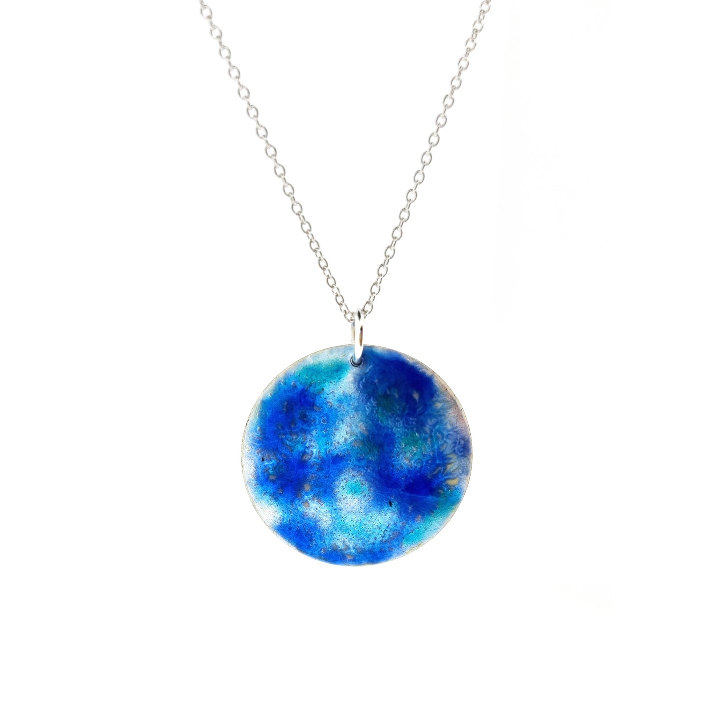 A round silver pendant with a mix of blue and turquoise enamel galaxy pattern on a silver chain.