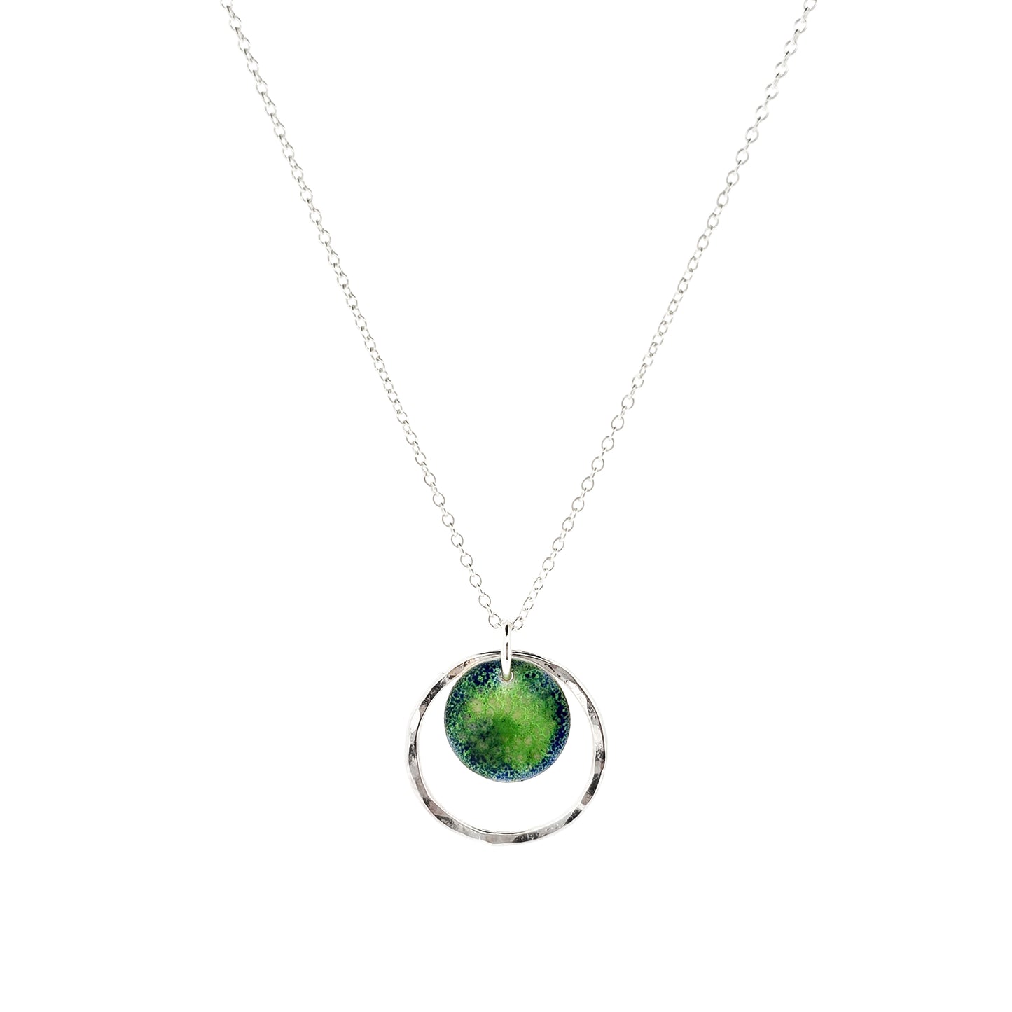 A silver pendant necklace featuring a silver disc with a pattern of green and blue enamel surrounded by a silver circle with a hammered finish. On a silver chain. 