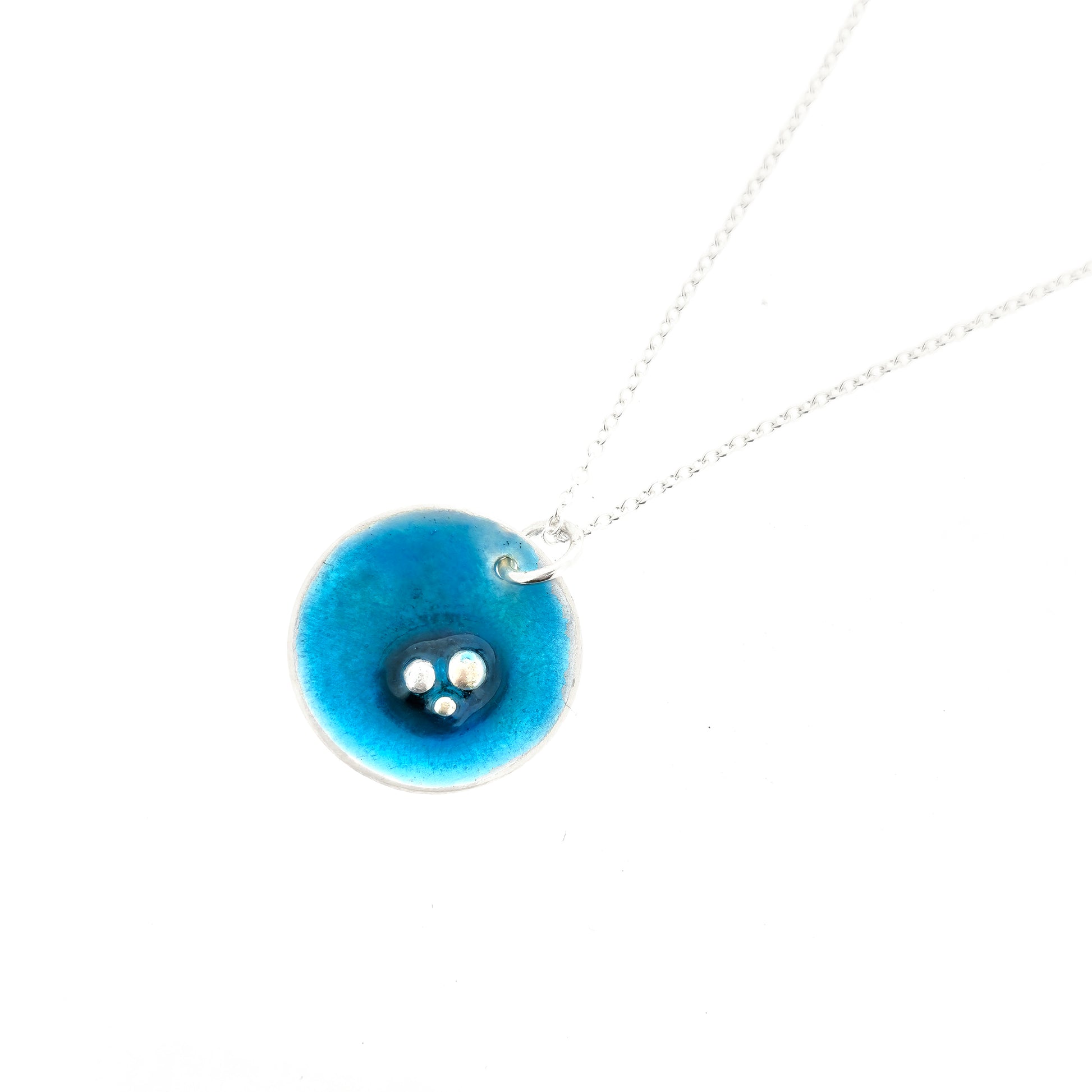 A round silver pendant on a silver chain. The pendant has 3 silver balls off-centre and is covered in turquoise blue enamel.