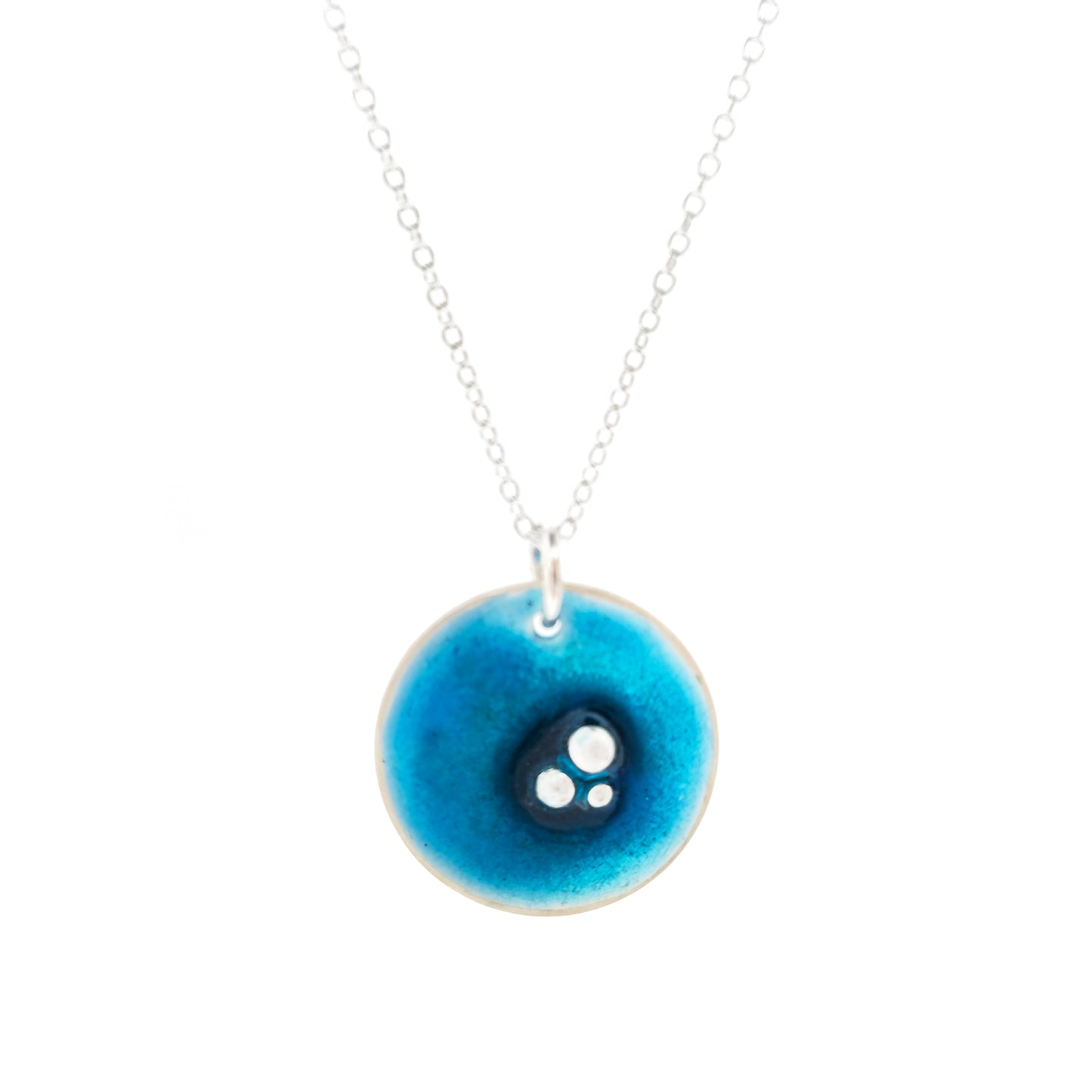 A round silver pendant on a silver chain. The pendant has 3 silver balls off-centre and is covered in turquoise blue enamel.