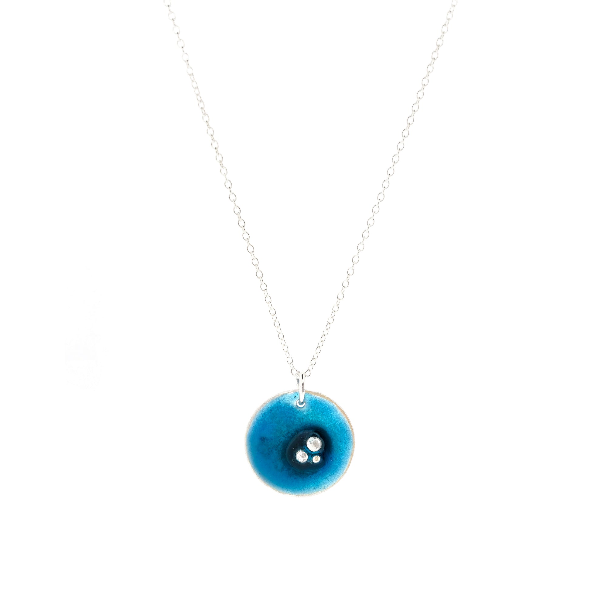 A round silver pendant on a silver chain. The pendant has 3 silver balls off-centre and is covered in turquoise blue enamel.