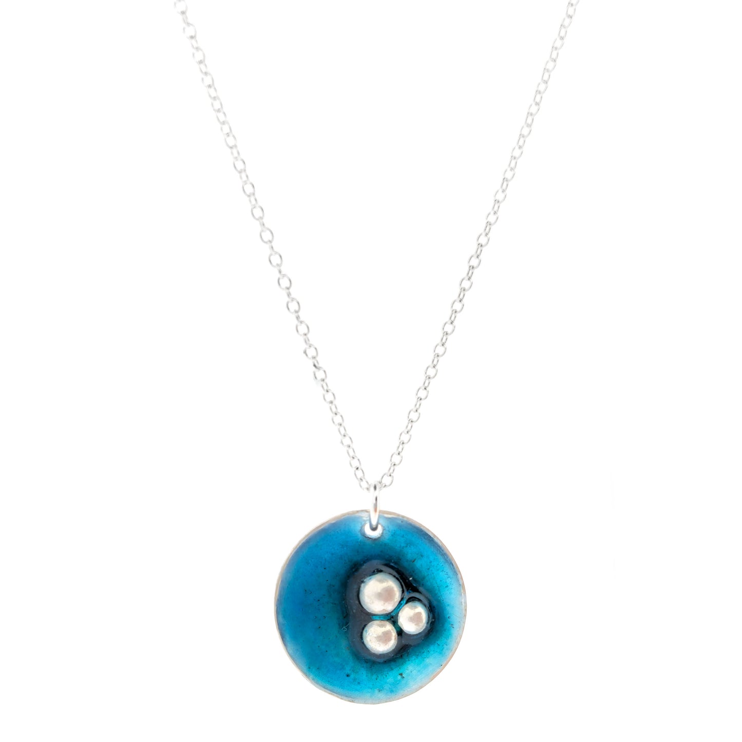 A handmade round silver pendant on a silver chain. The pendant has 3 silver balls off-centre and is covered in turquoise blue enamel. Mijoux Jewellery.
