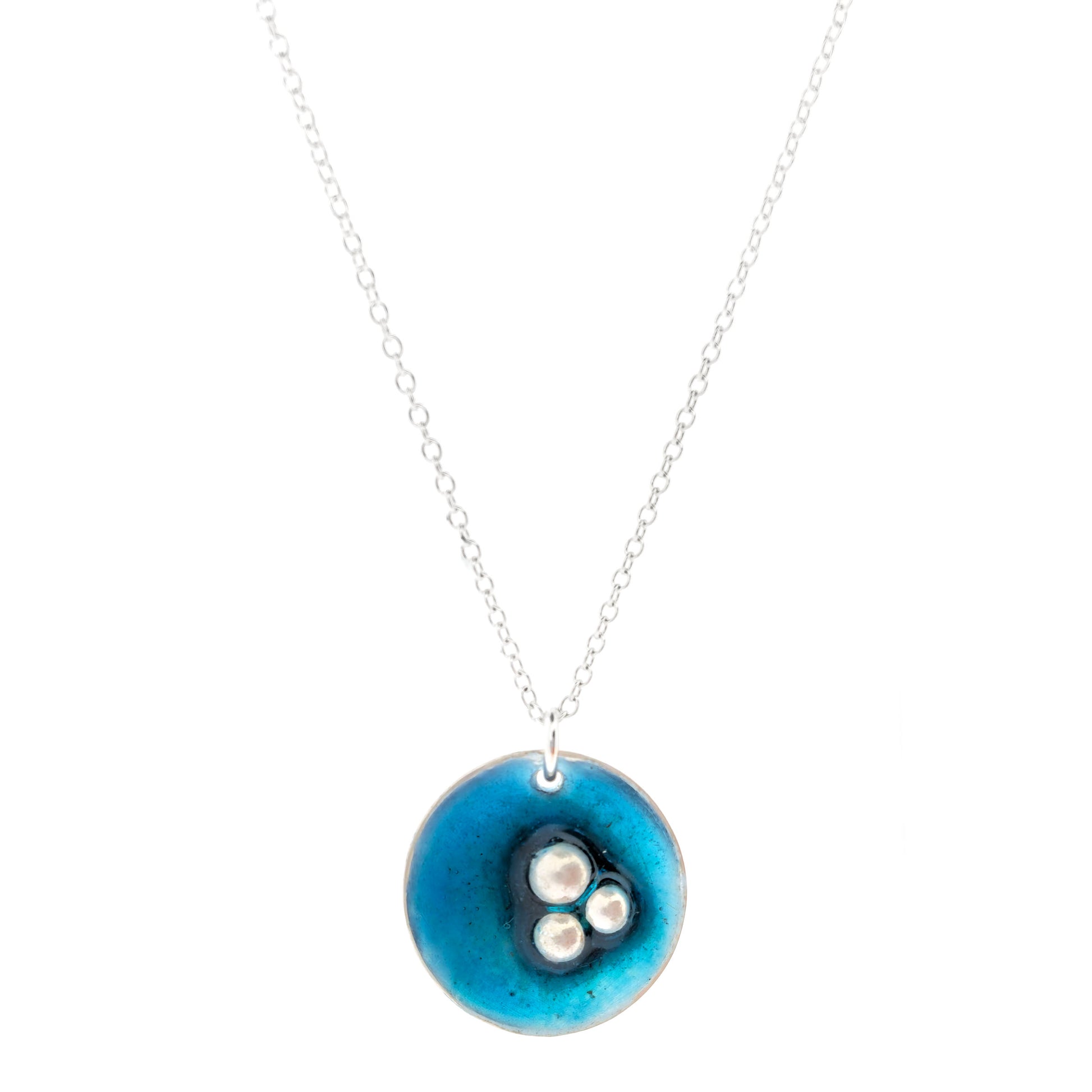 A handmade round silver pendant on a silver chain. The pendant has 3 silver balls off-centre and is covered in turquoise blue enamel. Mijoux Jewellery.