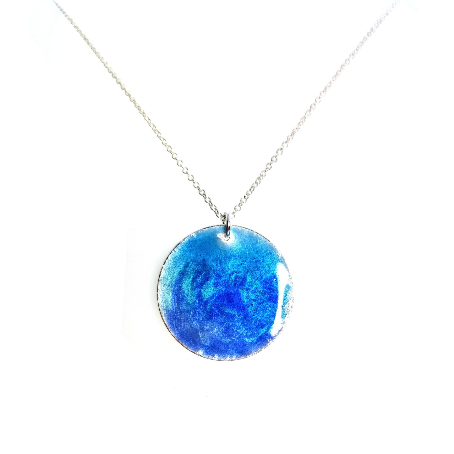 A round silver pendant with a mix of light and dark blue enamel suspended from a silver chain. - large