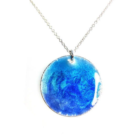 A round silver pendant with a mix of light and dark blue enamel suspended from a silver chain. - large