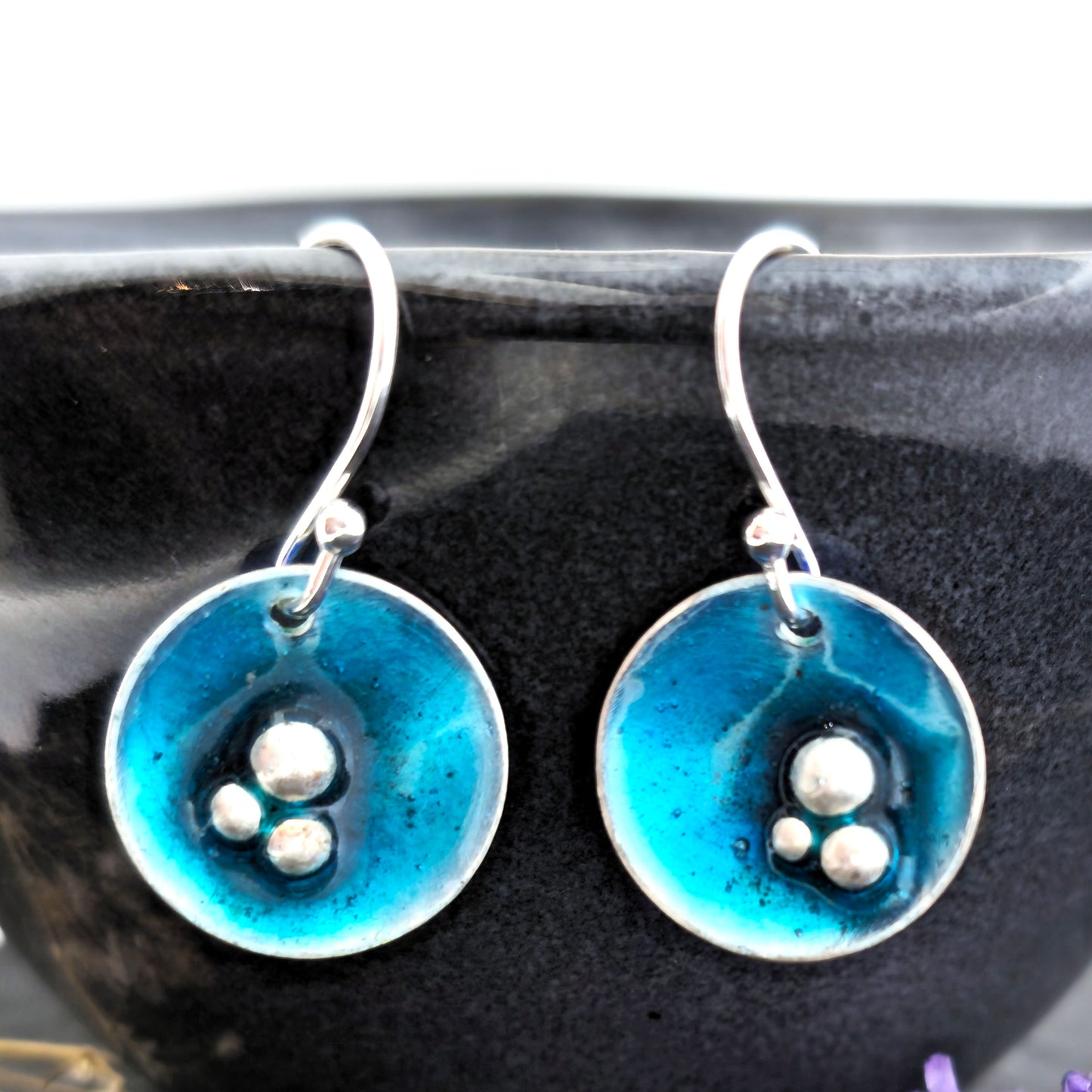 Handmade round silver drop earrings. Each earring has 3 silver balls off-centre and a turquoise blue enamel. Suspended from silver ear hooks. Mijoux Jewellery.