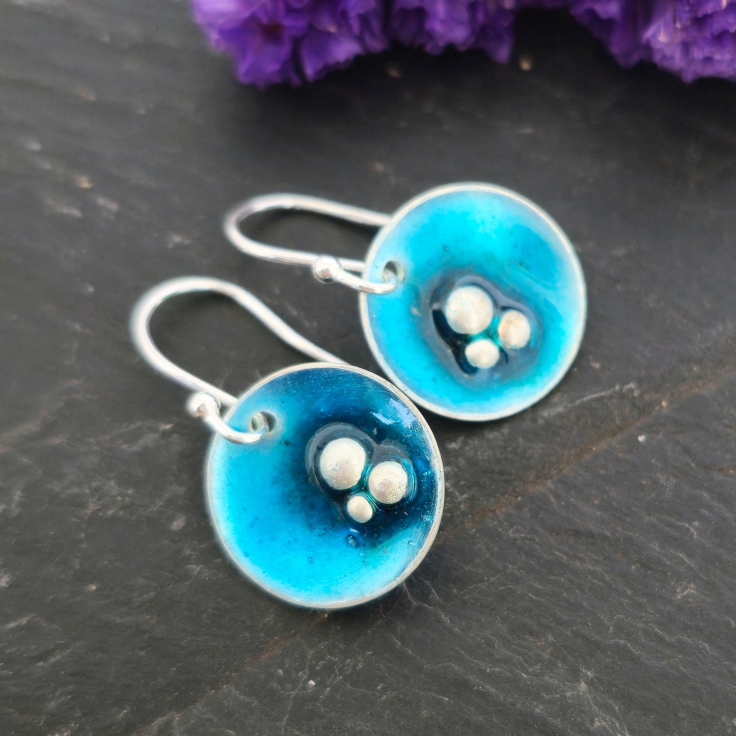 Handmade round silver drop earrings. Each earring has 3 silver balls off-centre and a turquoise blue enamel. Suspended from silver ear hooks. Mijoux Jewellery.