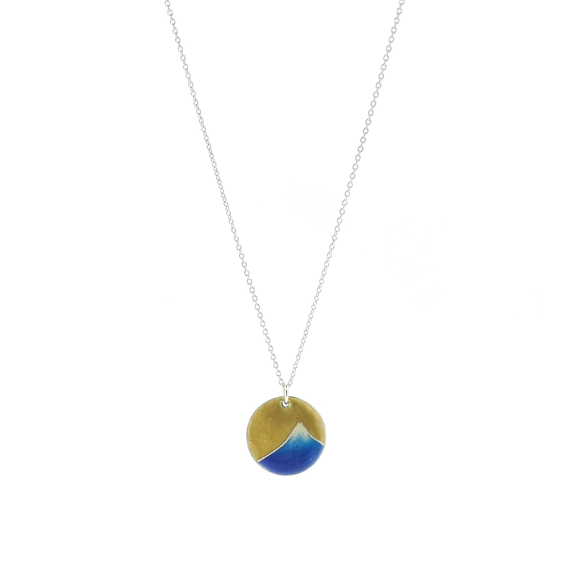 A round silver pendant with a graduated blue enamel mountain and a yellow enamel background. On a silver chain.