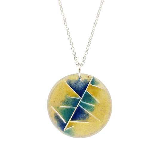 A round silver pendant with abstract silver lines and blue and turquoise enamels blending into pale yellow. Suspended from a silver chain.