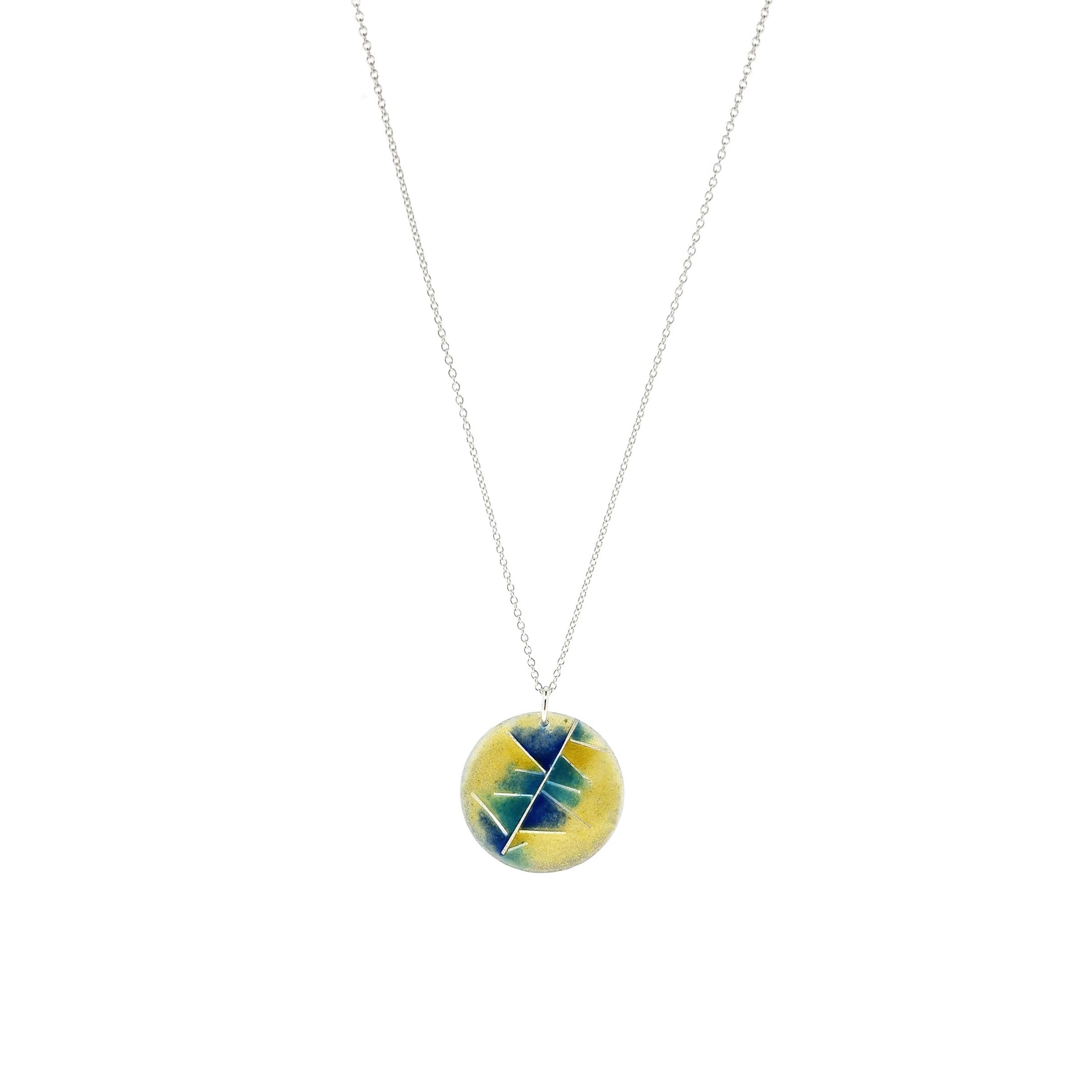 A round silver pendant with abstract silver lines and blue and turquoise enamels blending into pale yellow. Suspended from a silver chain.