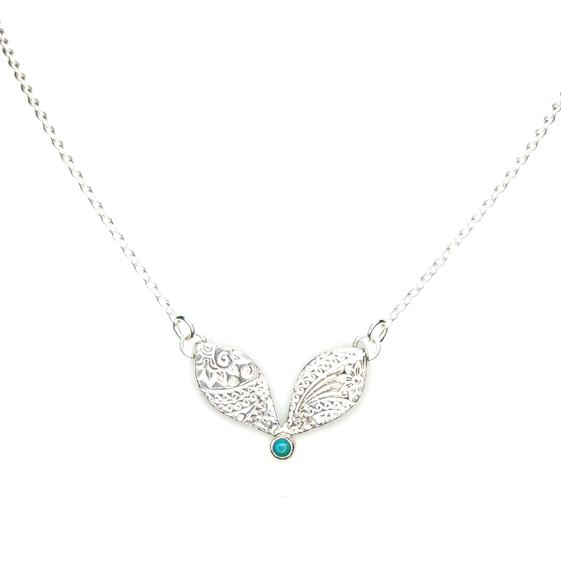 A silver necklace with a focal patterned element set with a turquoise gemstone.