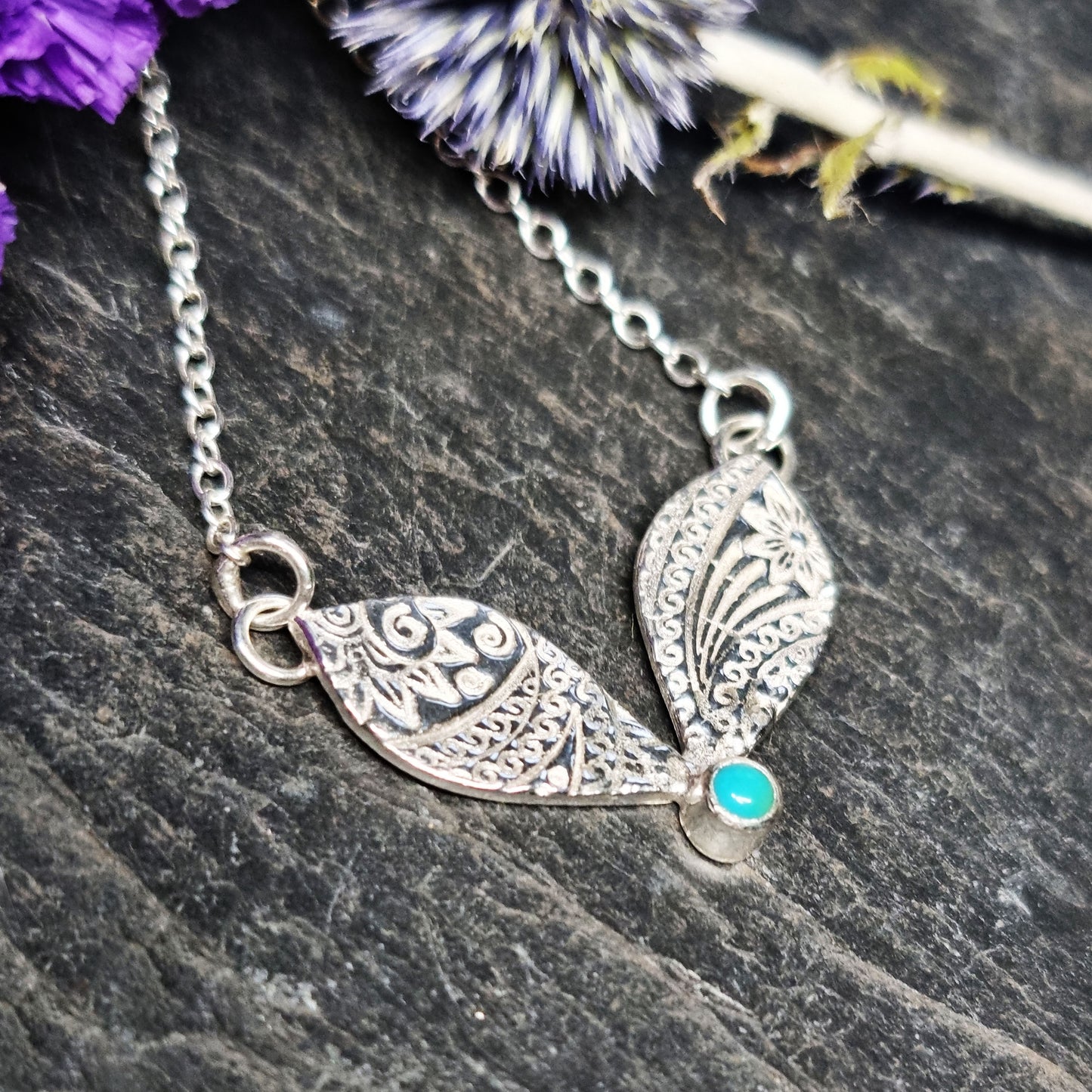 A silver necklace with a focal patterned element set with a turquoise gemstone with flowers