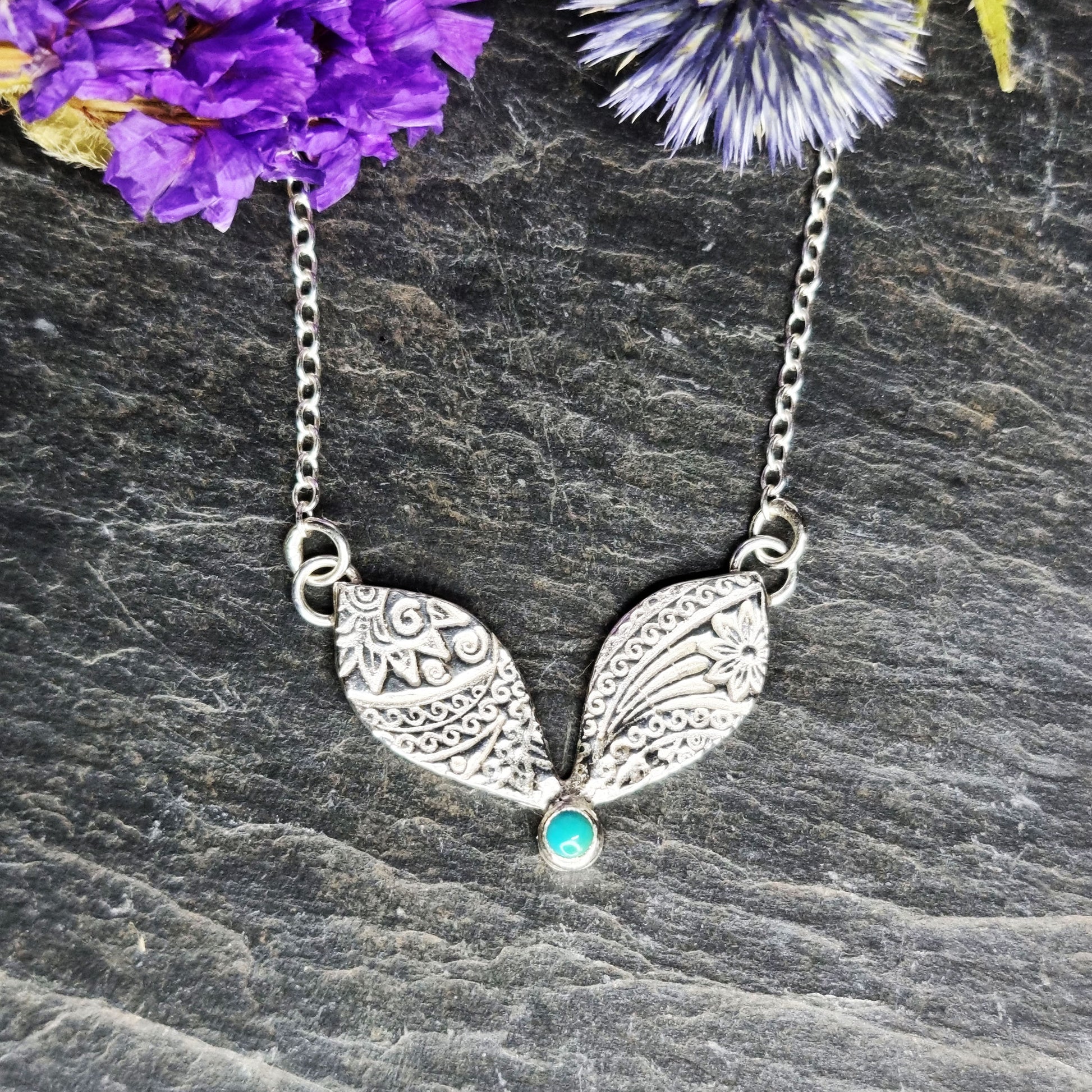 A silver necklace with a focal patterned element set with a turquoise gemstone with flowers