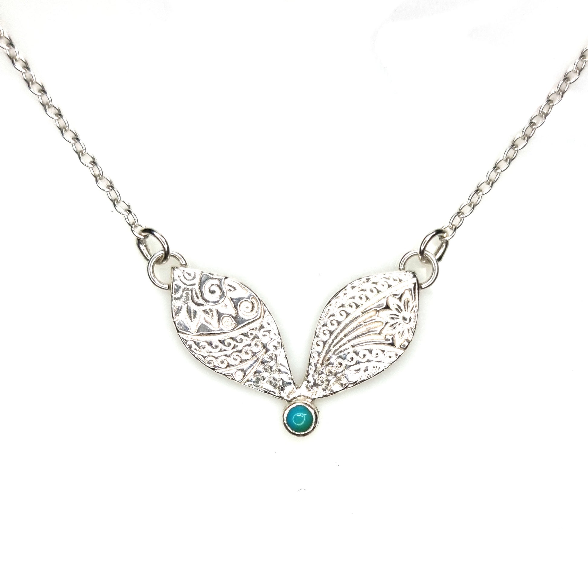 A silver necklace with a focal patterned element set with a turquoise gemstone.