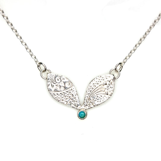 A silver necklace with a focal patterned element set with a turquoise gemstone.