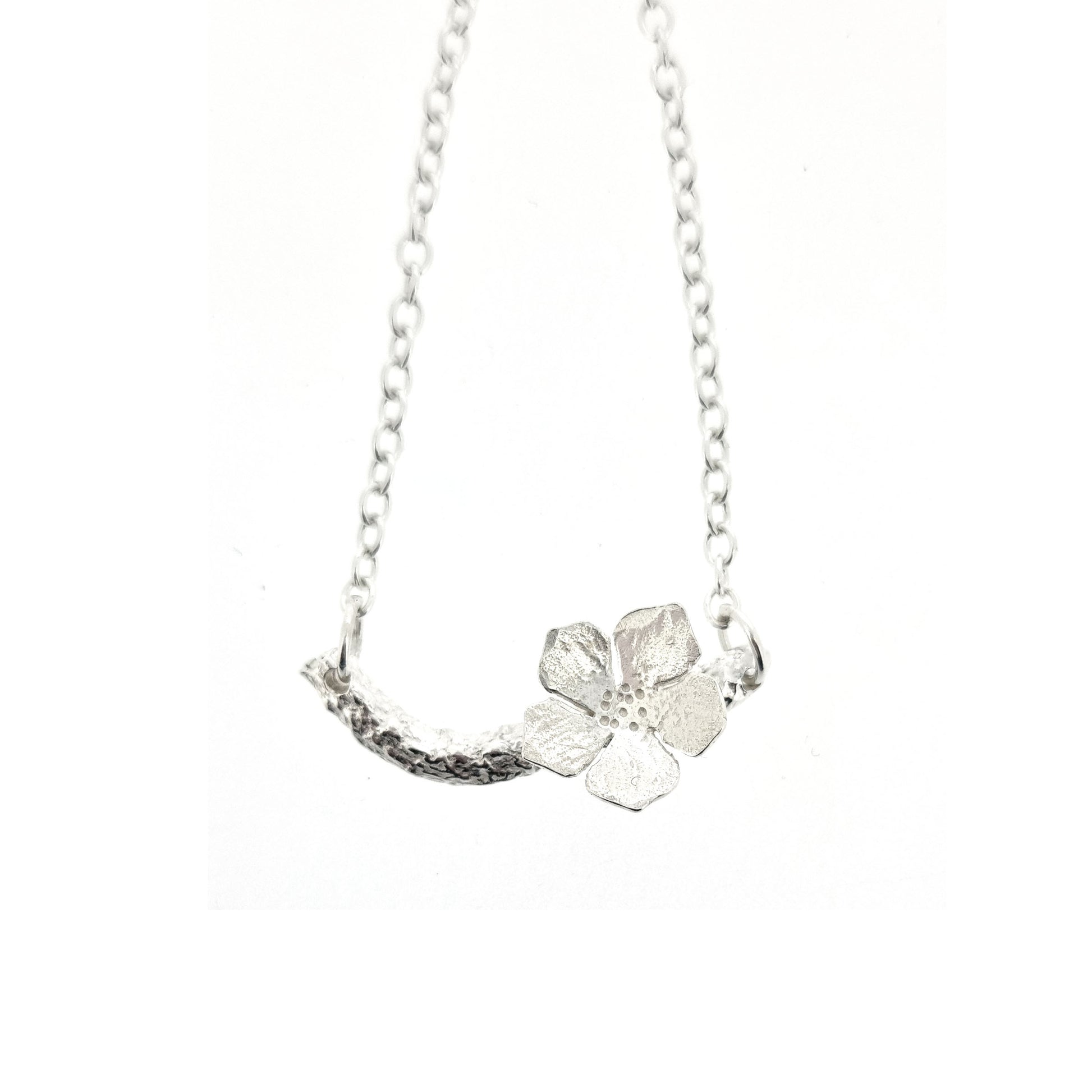 Silver necklace with small branch and a single 5 petal flower on it.