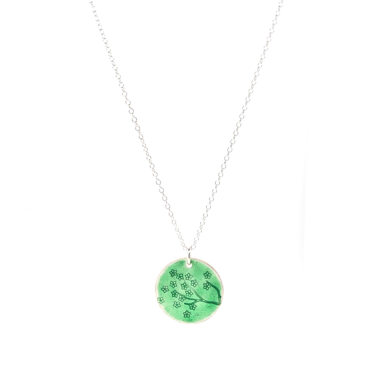 Silver necklace with a round green enamel pendant featuring floral designs on a white background.