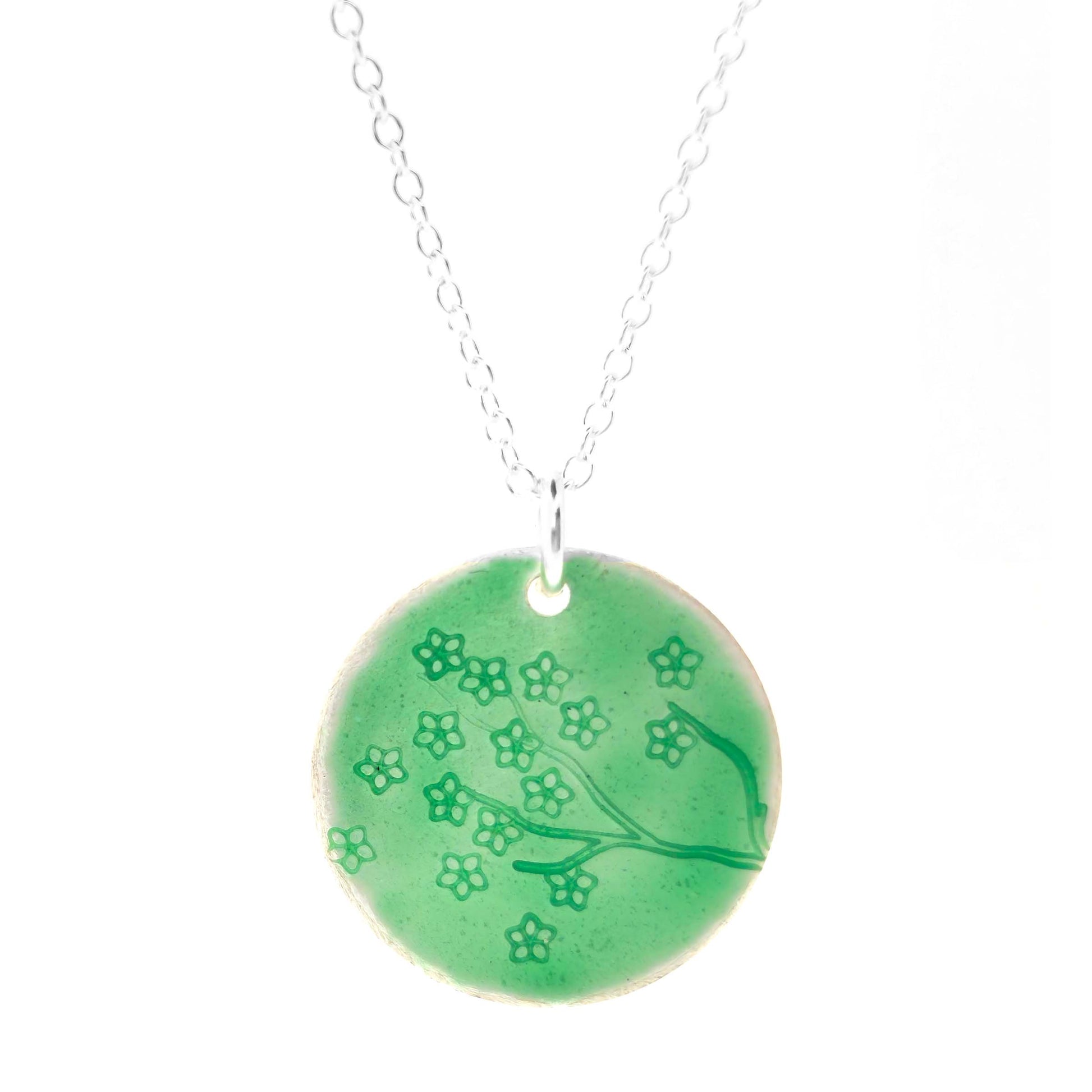Silver necklace with a round green enamel pendant featuring floral designs on a white background.