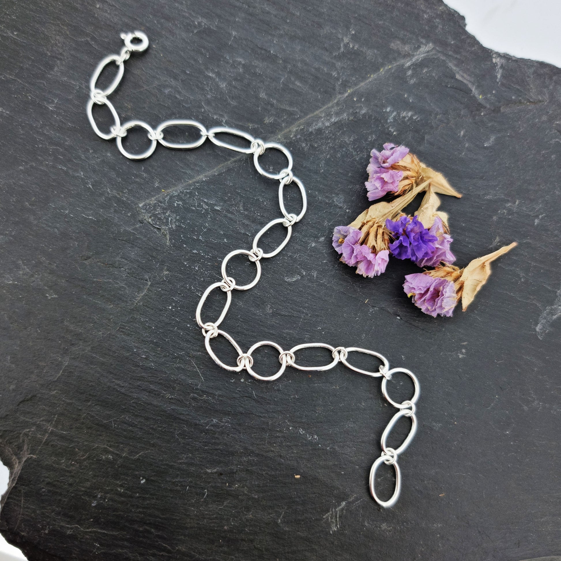 Silver chain link bracelet made of oval and circle links. Pictured with flowers.