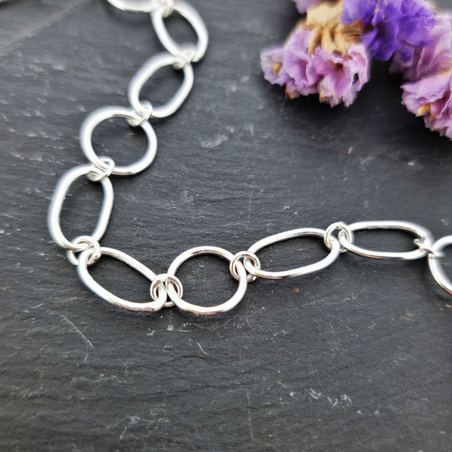 Silver chain link bracelet made of oval and circle links. Pictured with flowers.